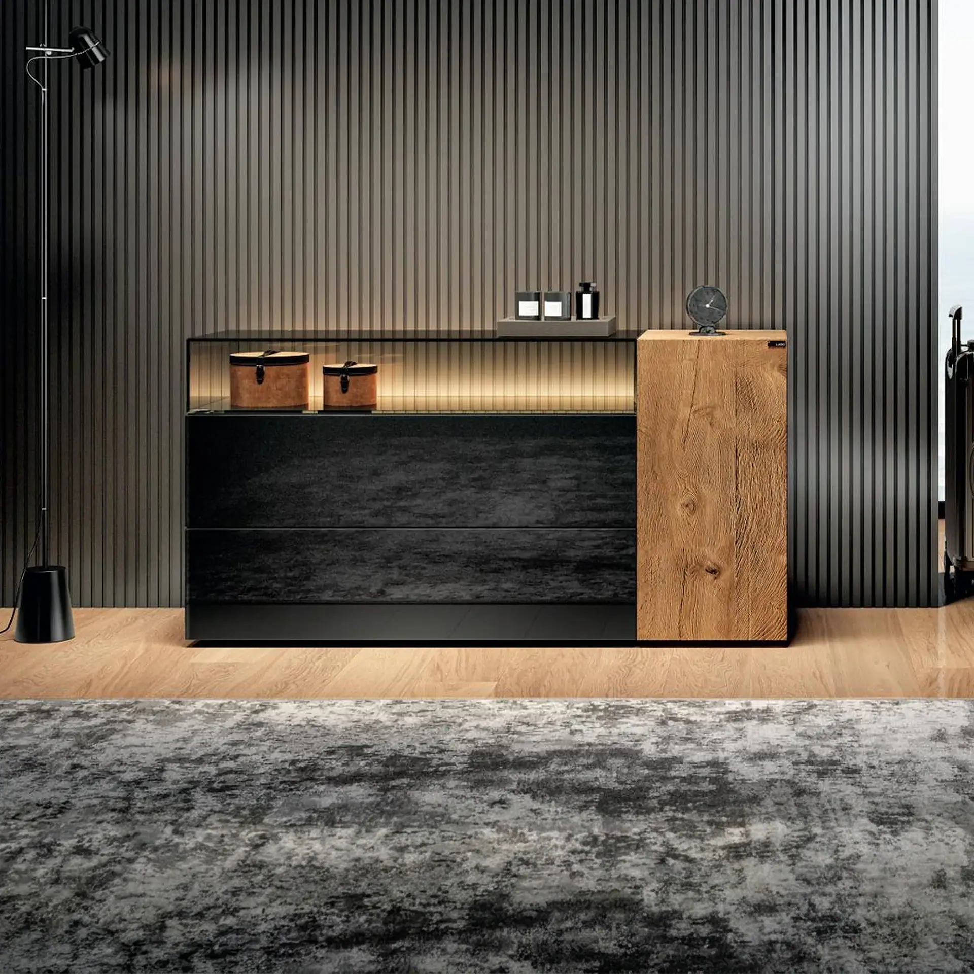 A modern black dresser with an illuminated glass top and a natural wood side cabinet, against a dark slatted wall. A floor lamp and patterned rug complete the contemporary interior.