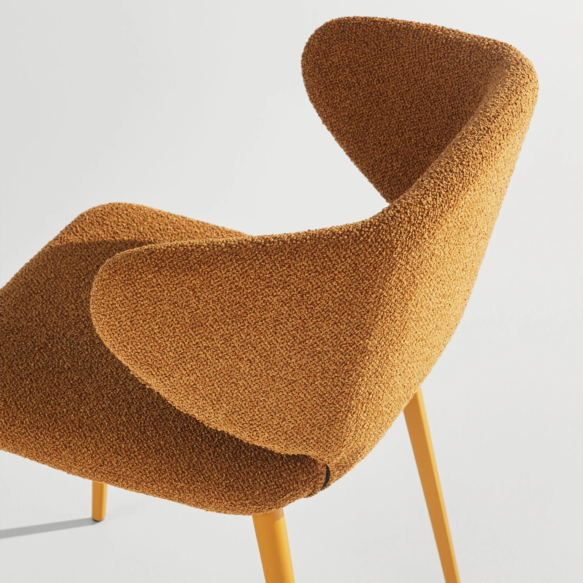A modern chair with orange-brown textured fabric upholstery and slender yellow legs, viewed from the back-right on a plain white background.