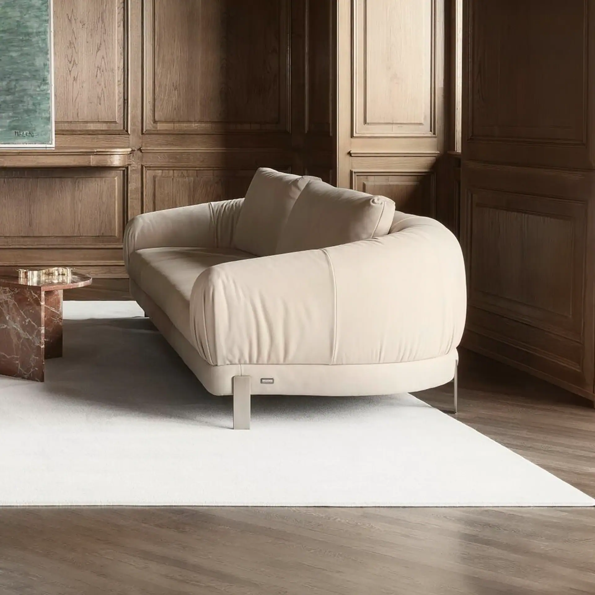 A light beige sofa with metal legs sits on a white rug in a room with dark wood paneling and a marble coffee table.