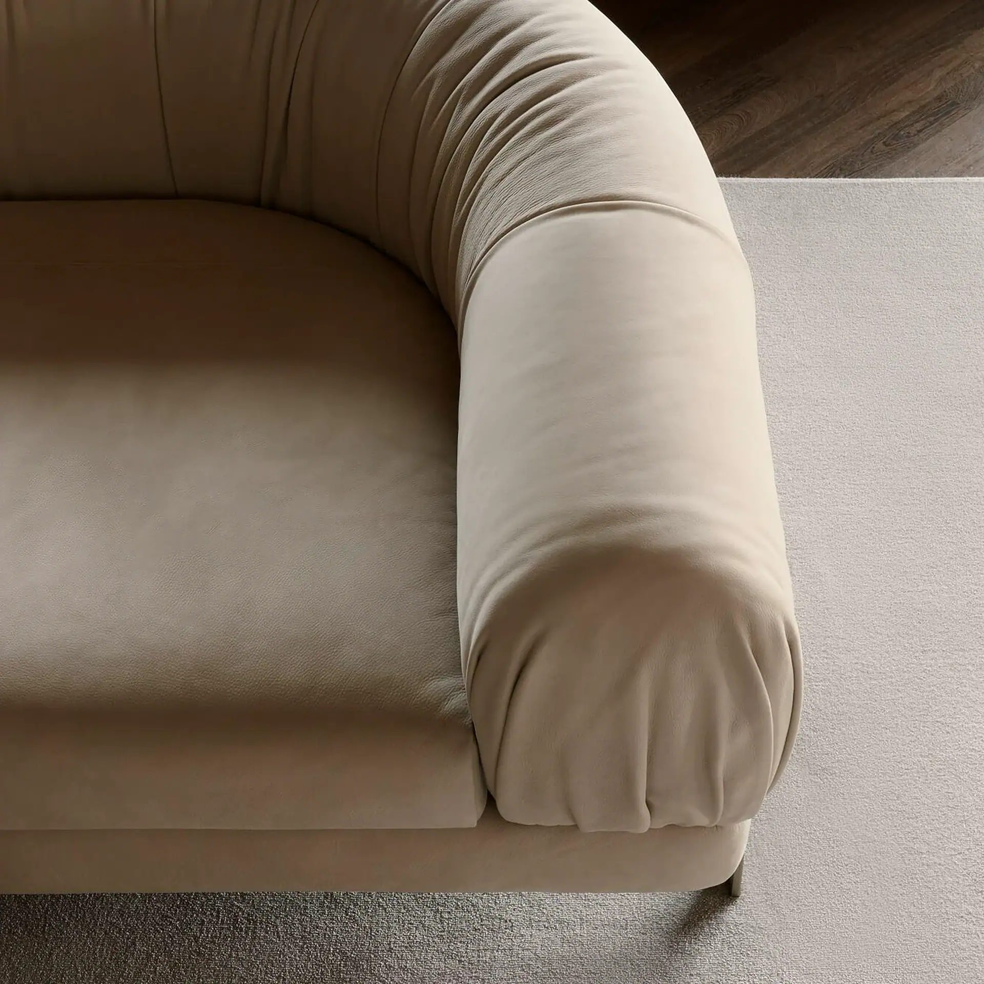 Close-up of a beige sofa with a rounded armrest and backrest, resting on a light gray carpet.