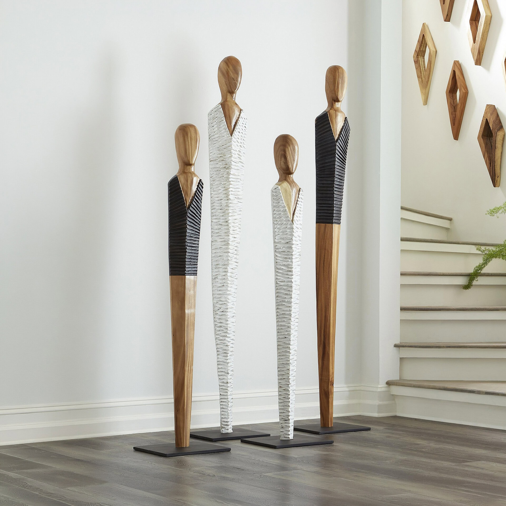 Vested wood sculpture art installation with elongated figures in a modern interior setting.