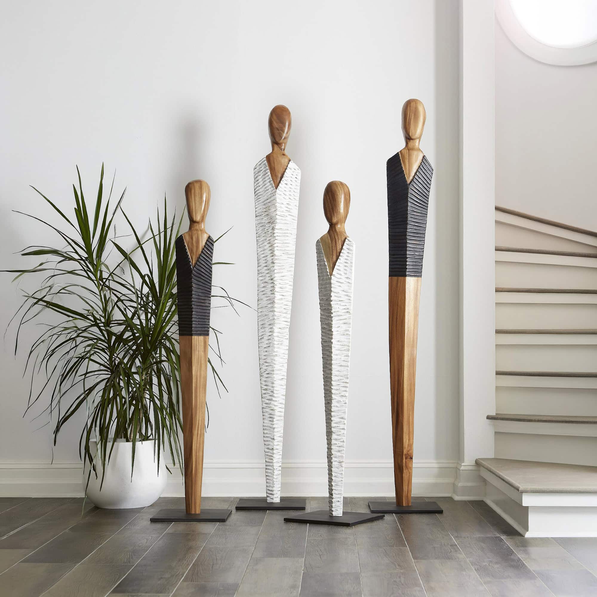 Vested wood sculpture art featuring elongated figures in a modern interior setting.