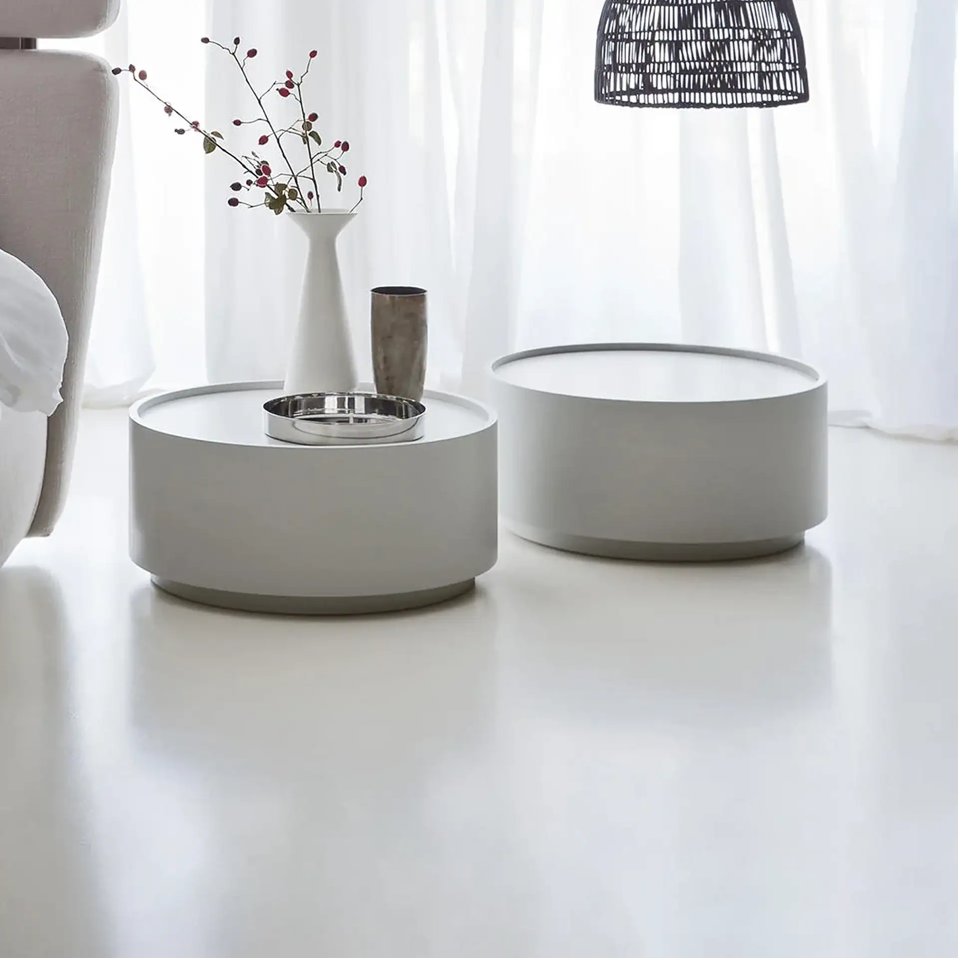 Two white round coffee tables in a bright living room with sheer curtains.