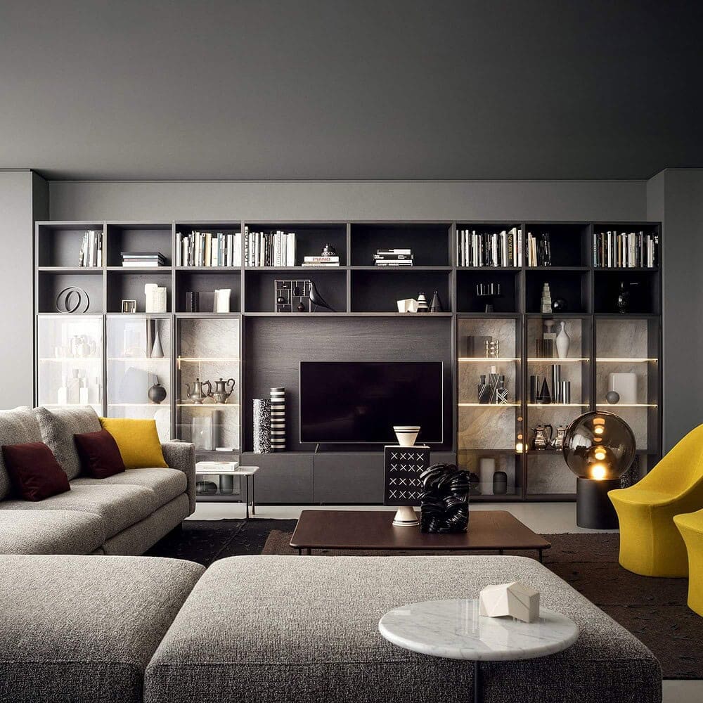 A modern living room with dark gray walls, a large built-in shelving unit with a TV, a light gray sectional sofa, and two bright yellow accent chairs.