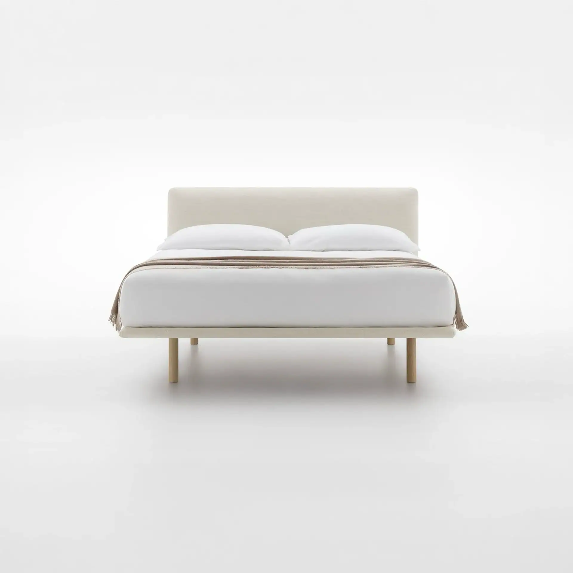 A minimalist bed with a light beige upholstered headboard and frame, white bedding, and a tan throw blanket, on a white background.