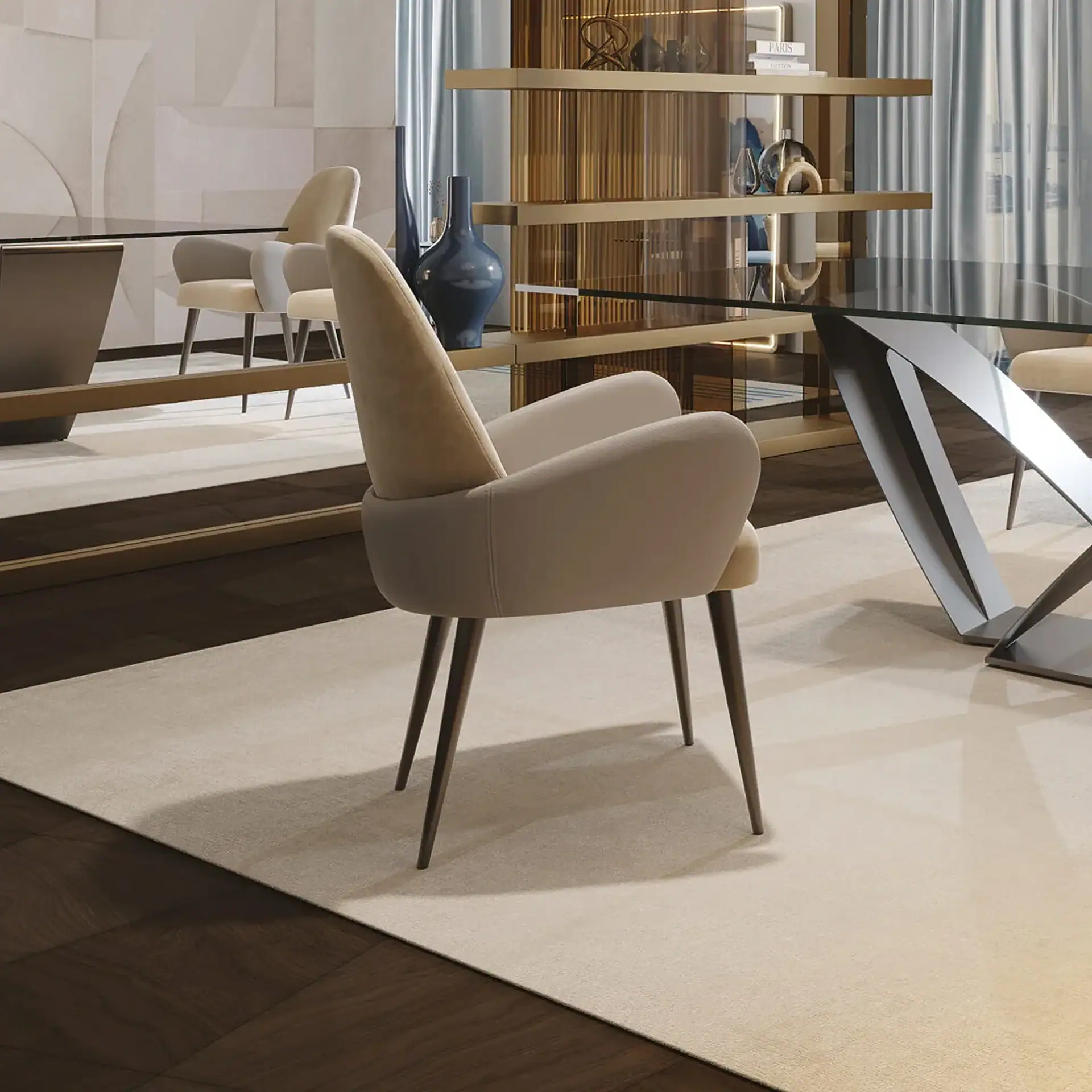 A modern dining room with a beige armchair on a light rug, a glass-top table, and gold-toned shelving with decor.
