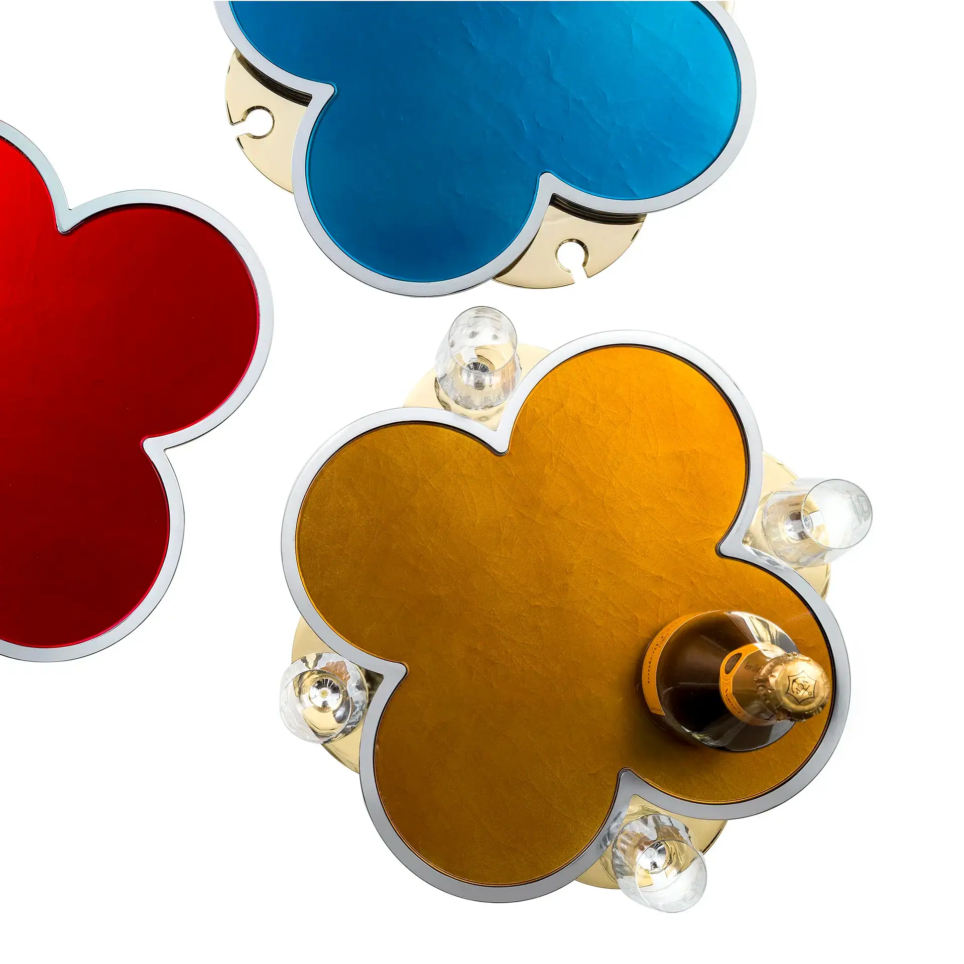 Three clover-shaped trays in red, blue, and gold. The gold tray holds a champagne bottle and three glasses.