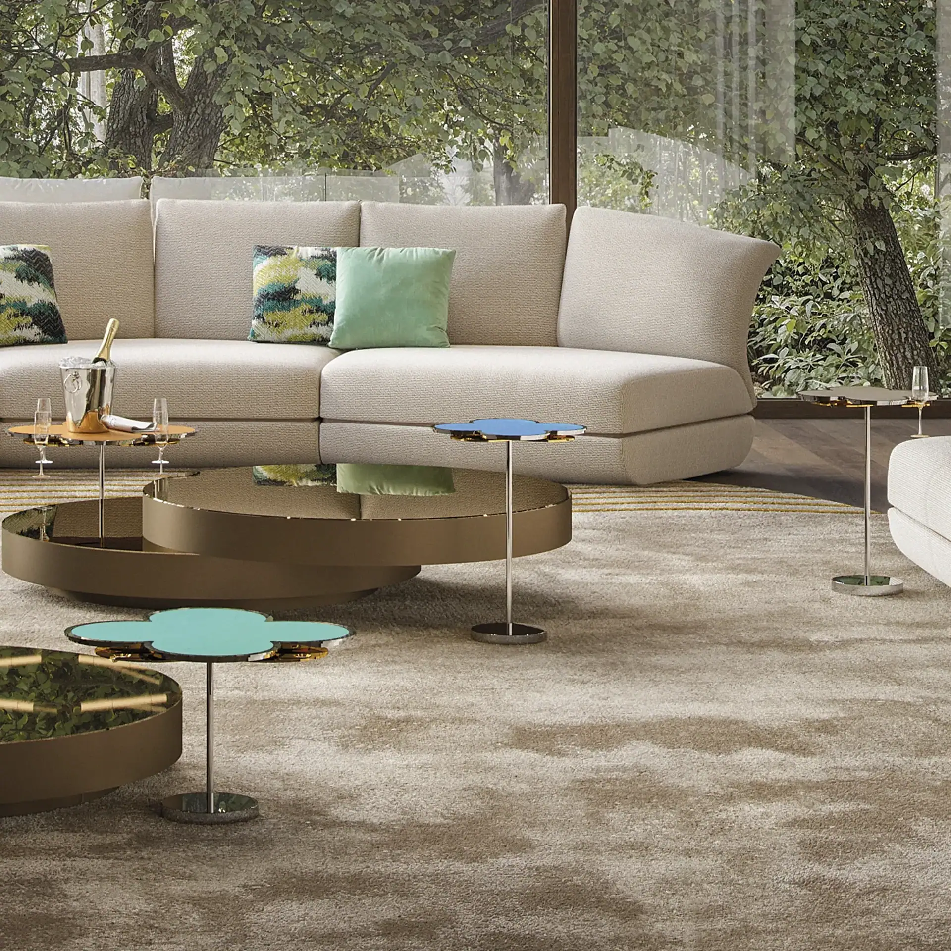 A modern living room with a beige sectional sofa, multiple coffee tables, and large windows overlooking green trees.