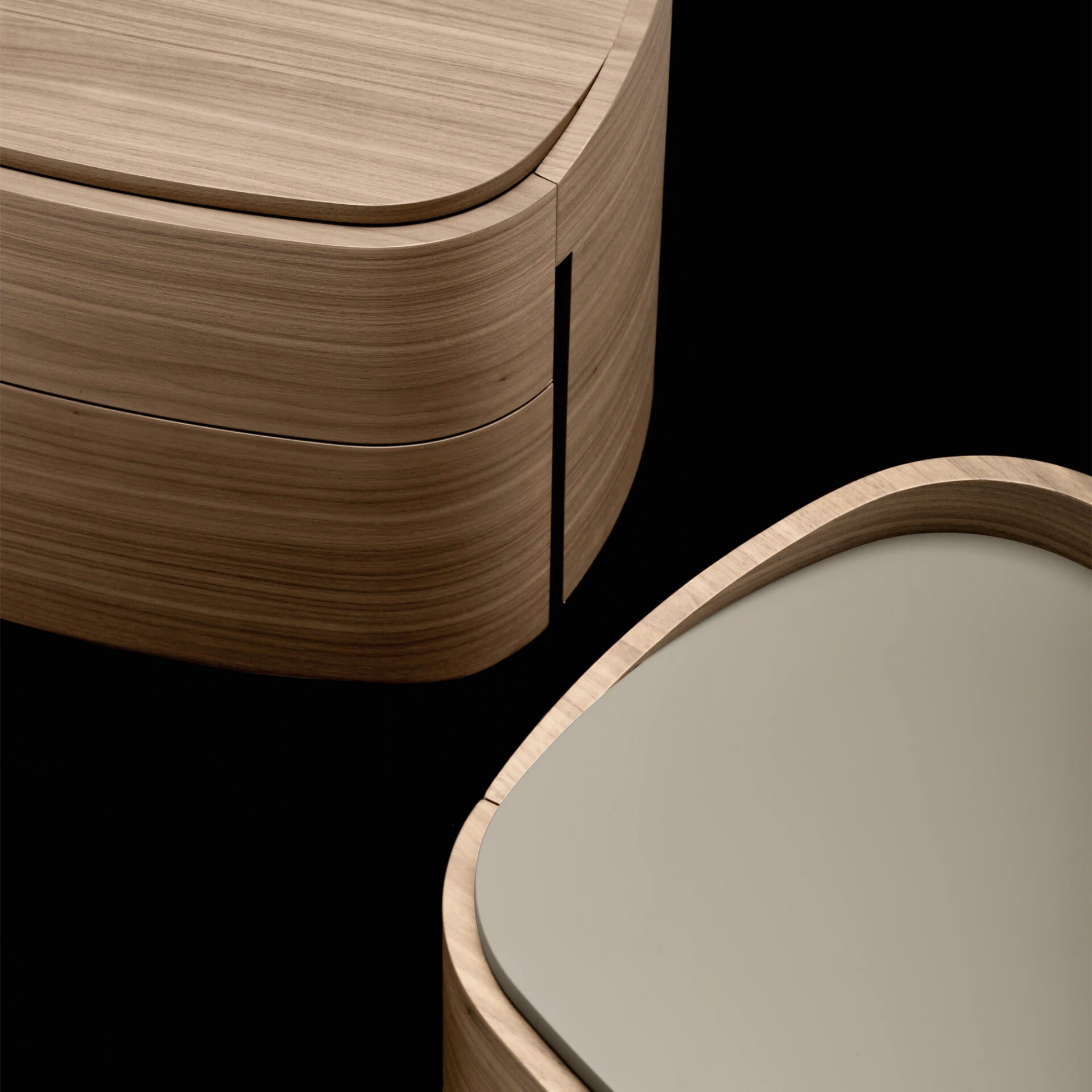 Close-up of two curved, light wood furniture pieces with natural grain, one with a multi-layered design and a vertical slit, the other with a light gray surface, against a black background.