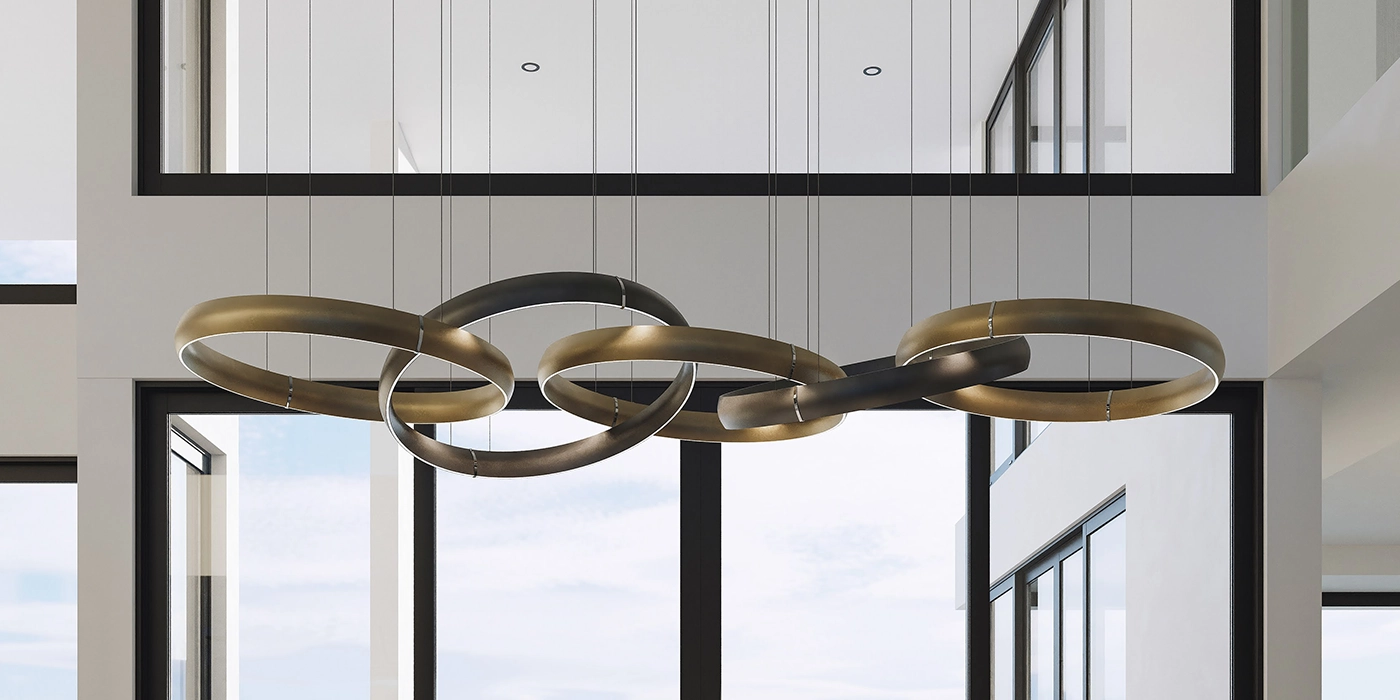 A modern, sculptural chandelier with interconnected, two-tone metallic rings emitting soft white light, suspended in a high-ceilinged room with large windows.