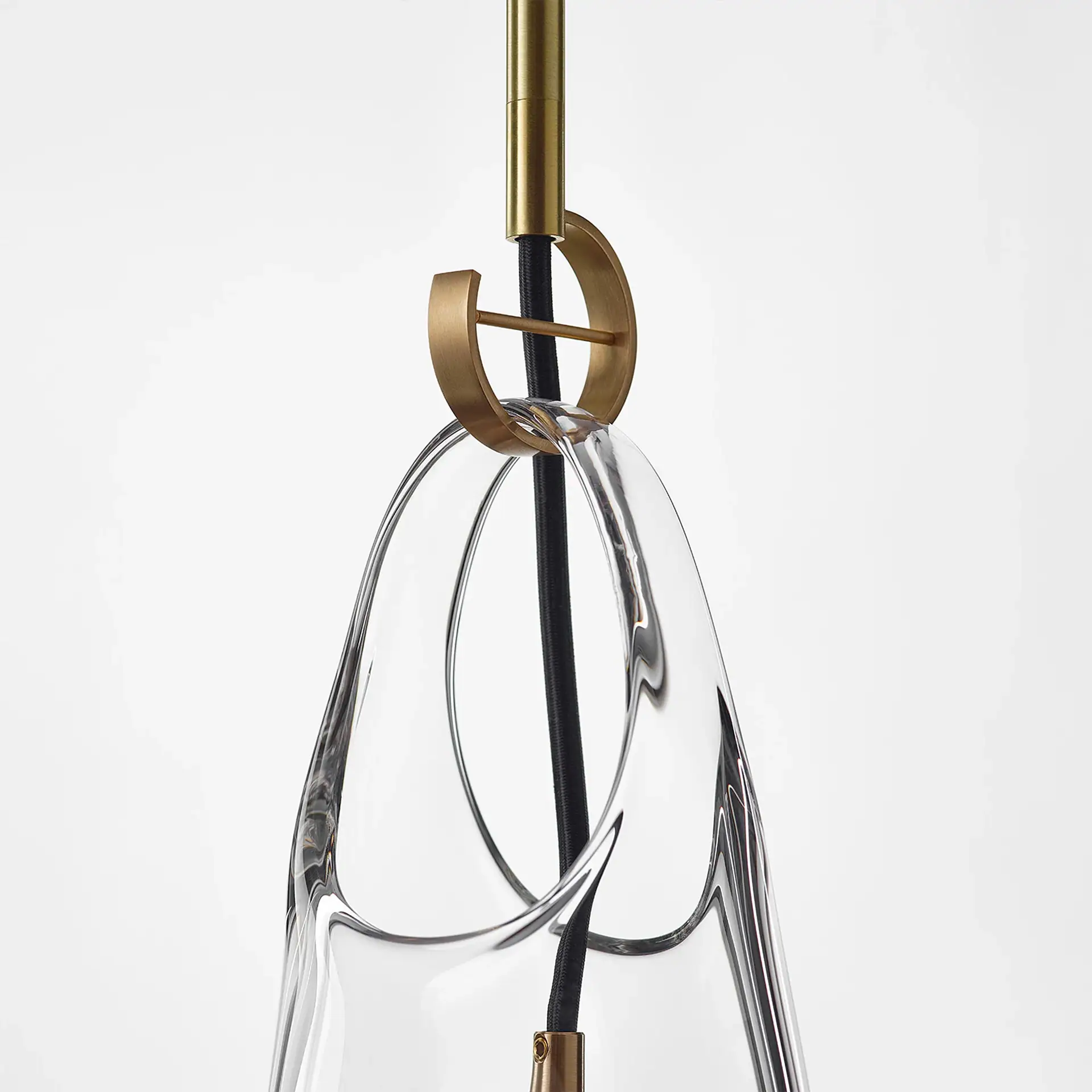 Close-up of a modern pendant light with a clear, irregularly shaped glass shade, suspended by a brass rod and a decorative brass ring, against a white background.