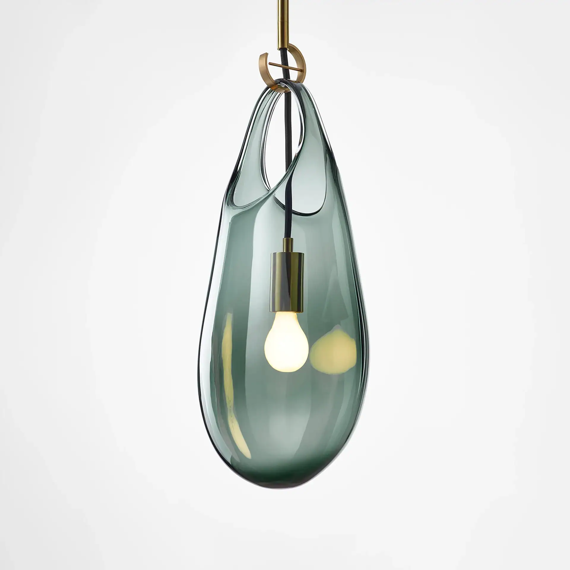 A modern pendant light with a translucent, dark teal teardrop-shaped glass shade, a glowing bulb inside, and brass suspension hardware, set against a white background.