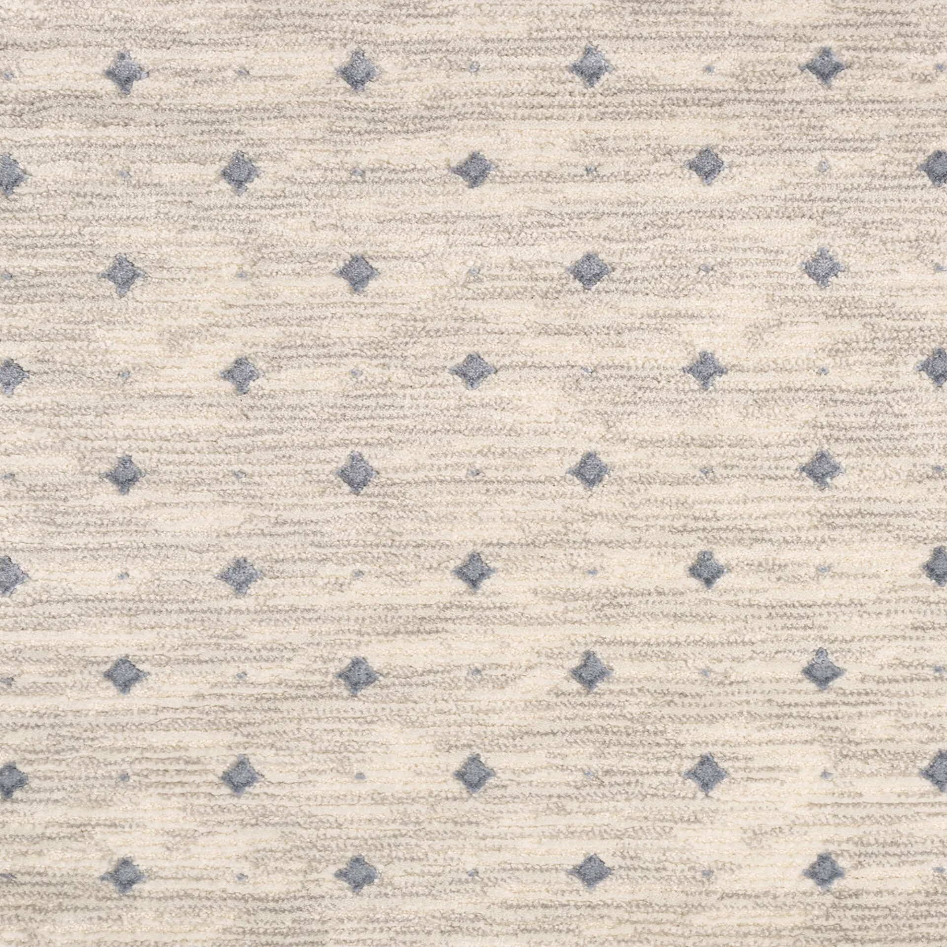 A close-up of a textured off-white rug with a repeating pattern of small, muted blue-gray diamonds and faint horizontal lines.