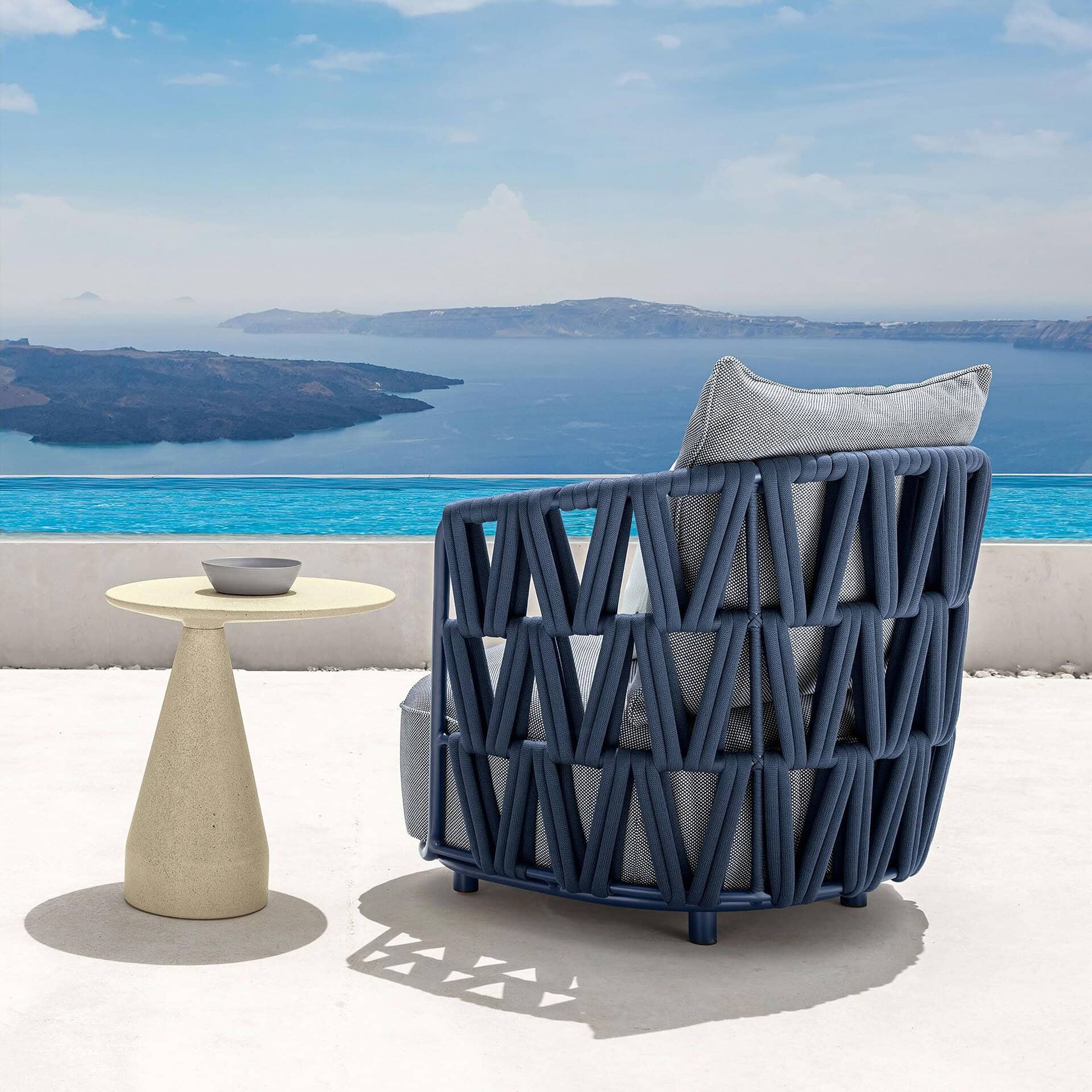 Outdoor lounge armchair with navy blue woven frame and light gray cushion.