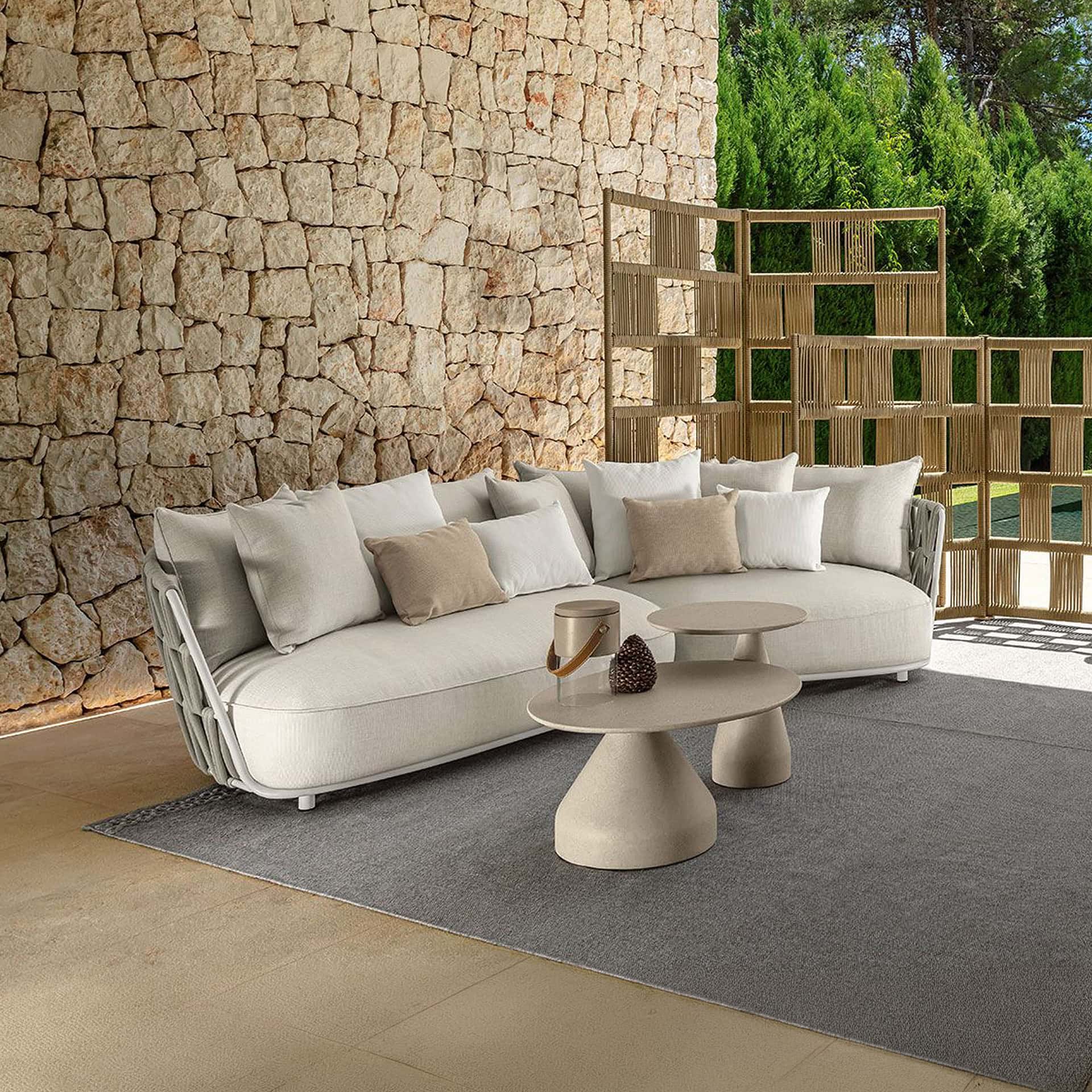 Stylish outdoor sectional sofa with neutral cushions on a patio with stone wall and greenery.