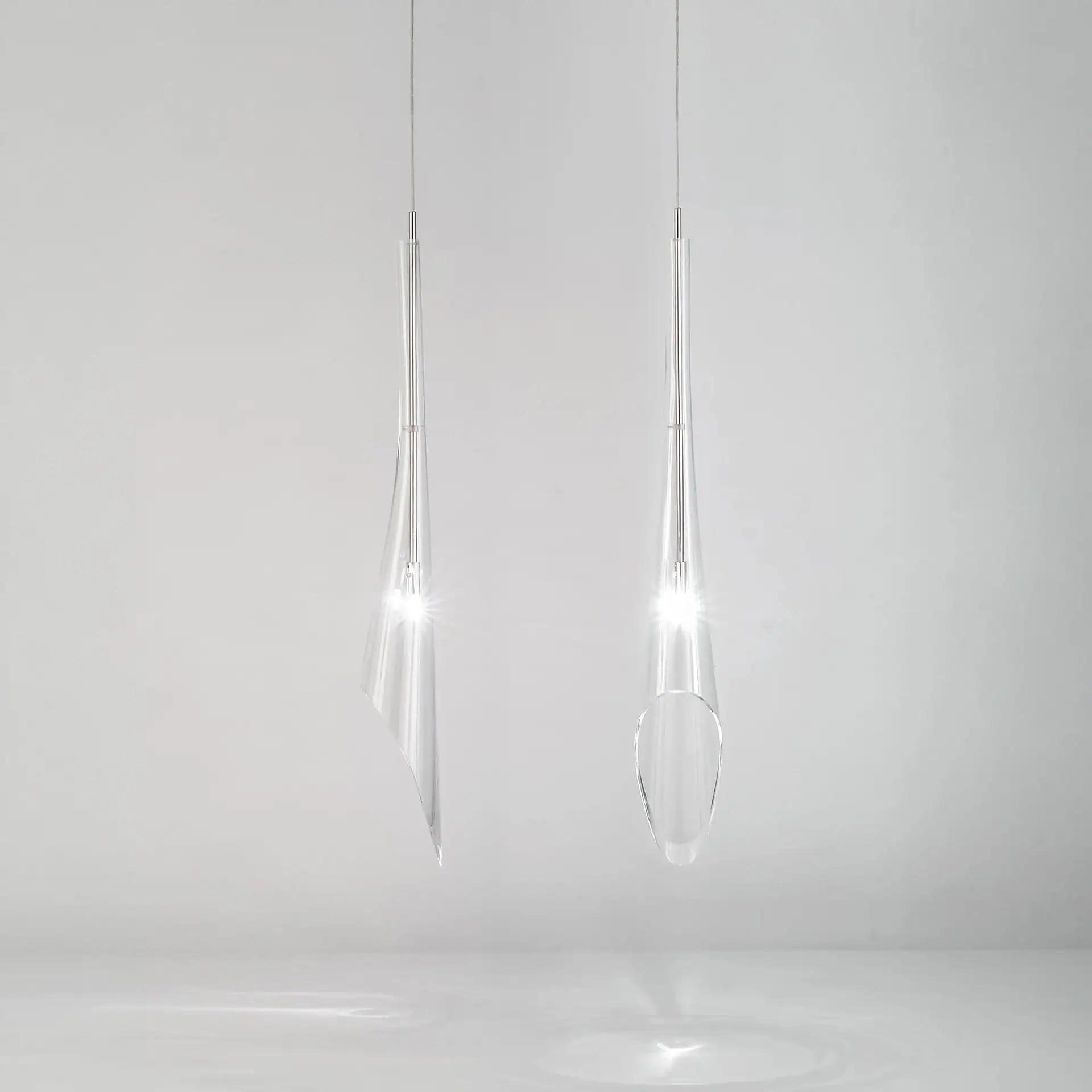 Two modern clear glass or acrylic pendant lights with bright internal light sources hang against a light gray background.
