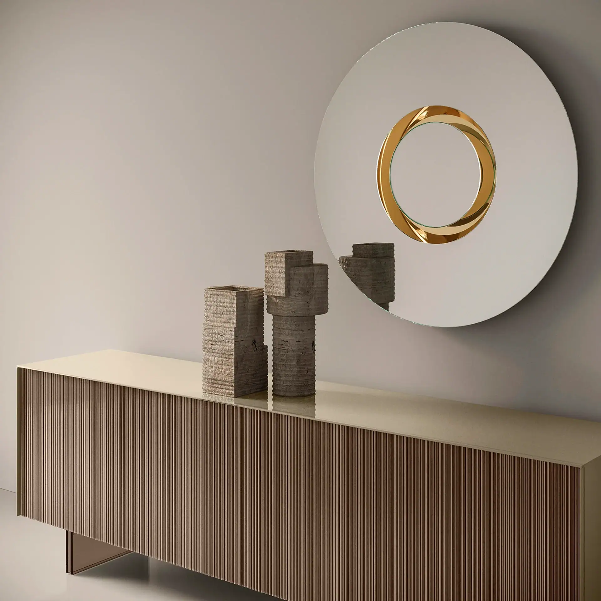 A modern interior with a ribbed sideboard, two textured concrete-like vases, and a large circular mirror with a golden twisted center.