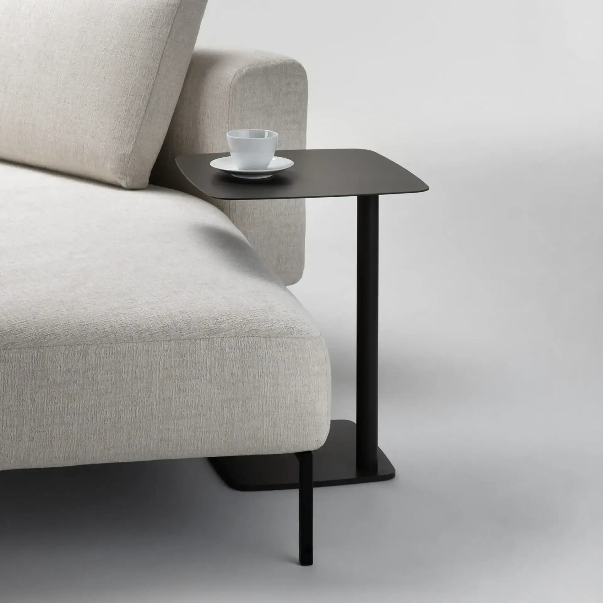 Modern beige sofa with black side table and coffee cup.