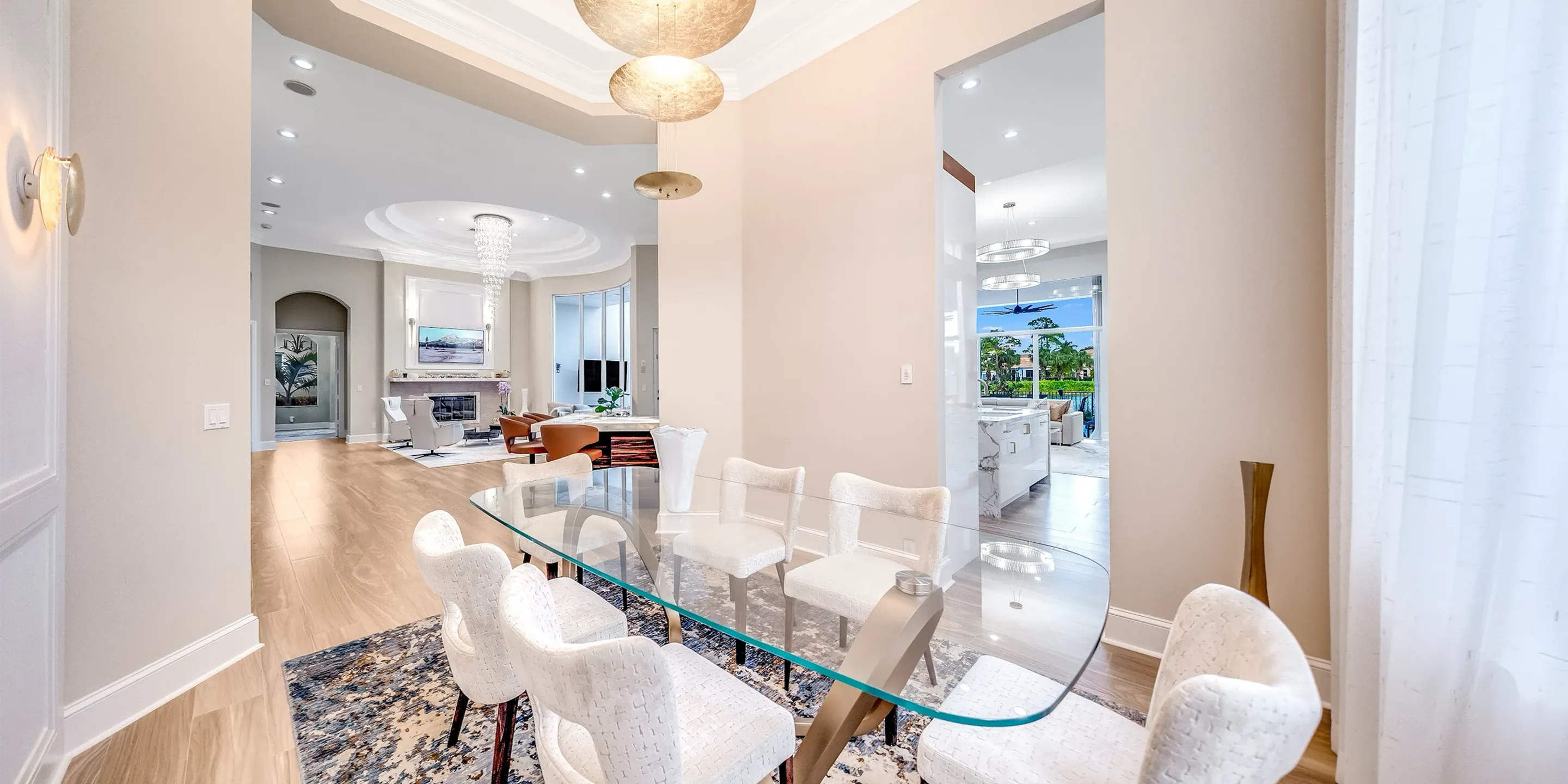 Elegant dining room with glass table and white upholstered chairs.