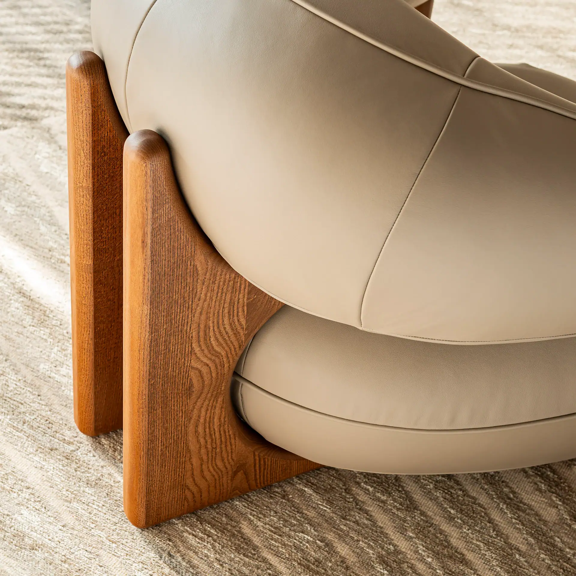 Close-up of the wooden base of the Ruby Lounge Armchair with beige upholstery.