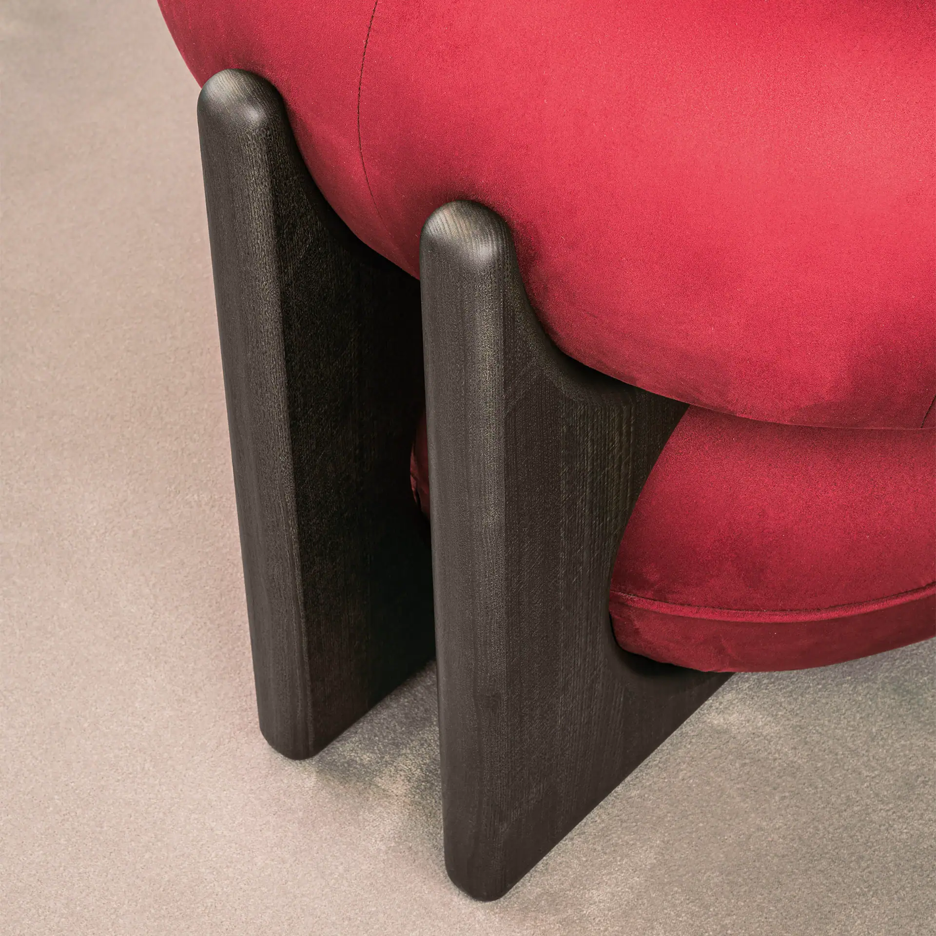 Close-up of Ruby Lounge Armchair with red fabric and dark wooden legs.
