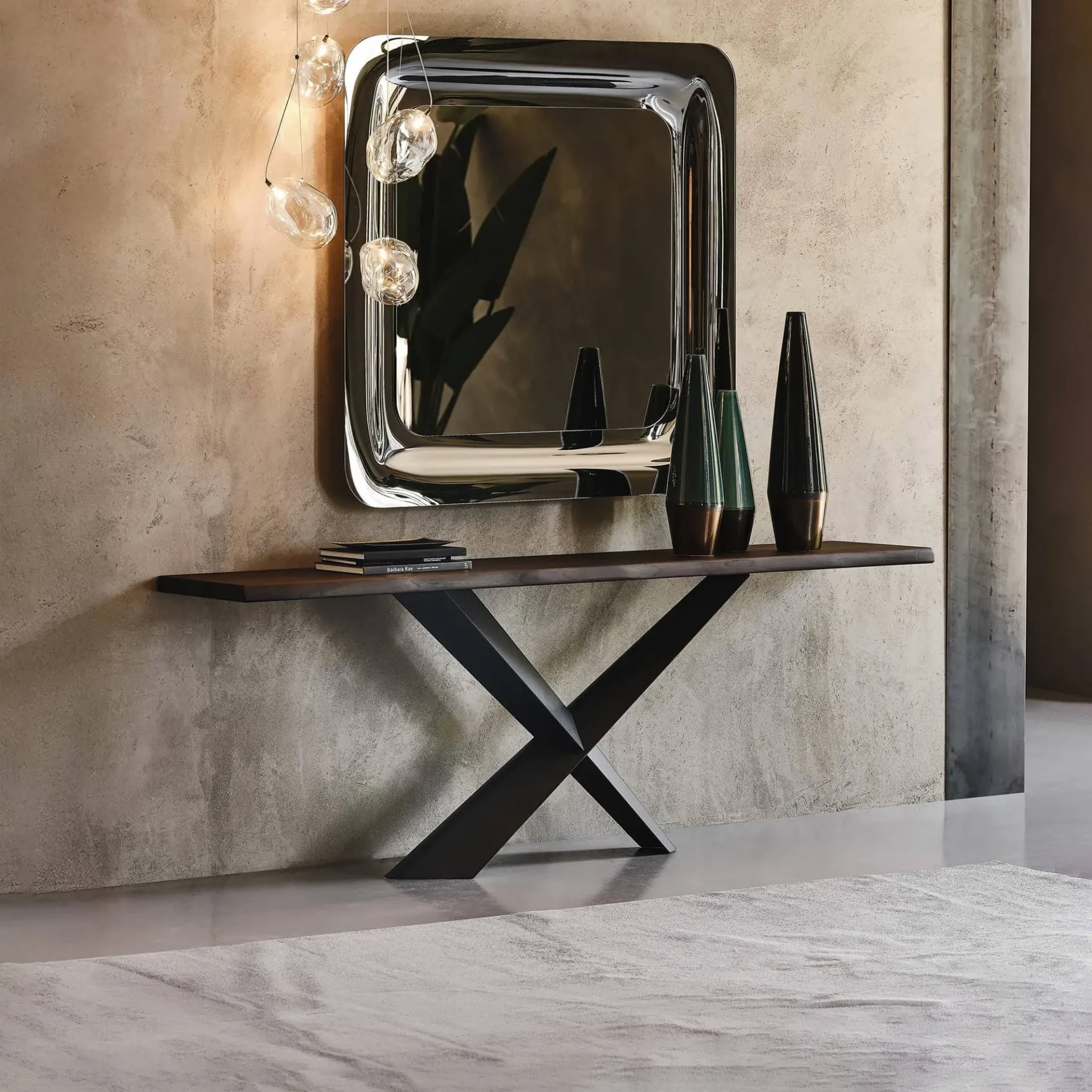 A modern console table with an X-shaped base, a large metallic mirror, and unique pendant lights in an entryway.