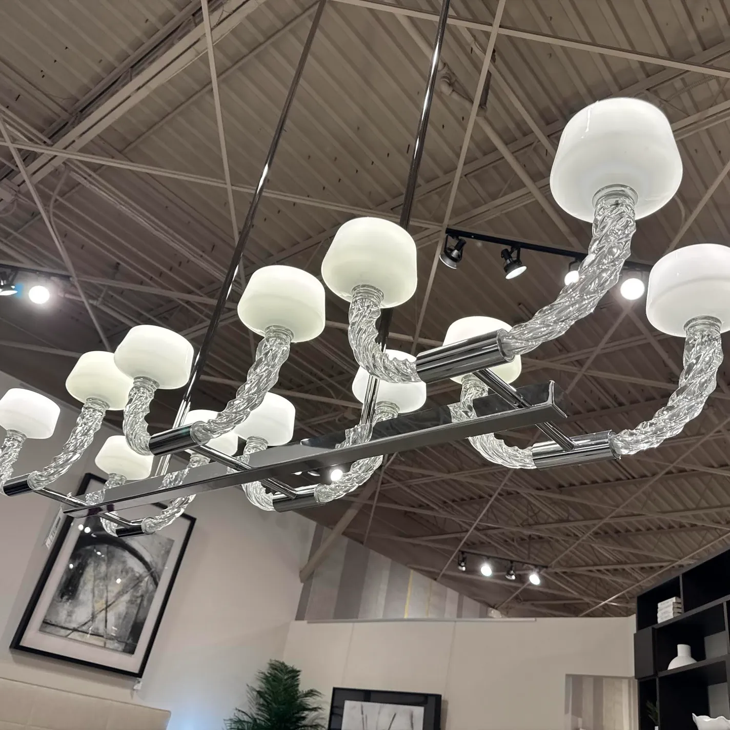 A modern chandelier with multiple white glass shades and twisted clear glass arms, suspended from an industrial ceiling with track lighting.