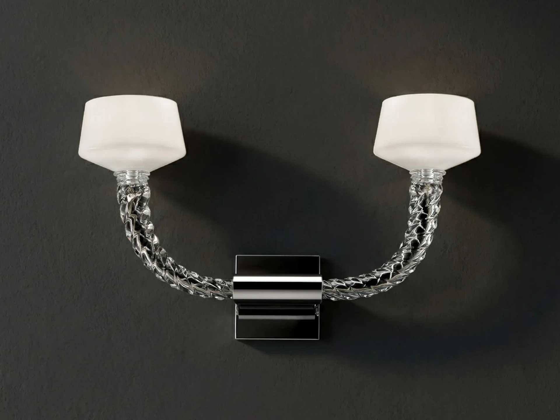 A U-shaped wall sconce with two frosted white shades and twisted clear glass arms mounted on a dark wall.