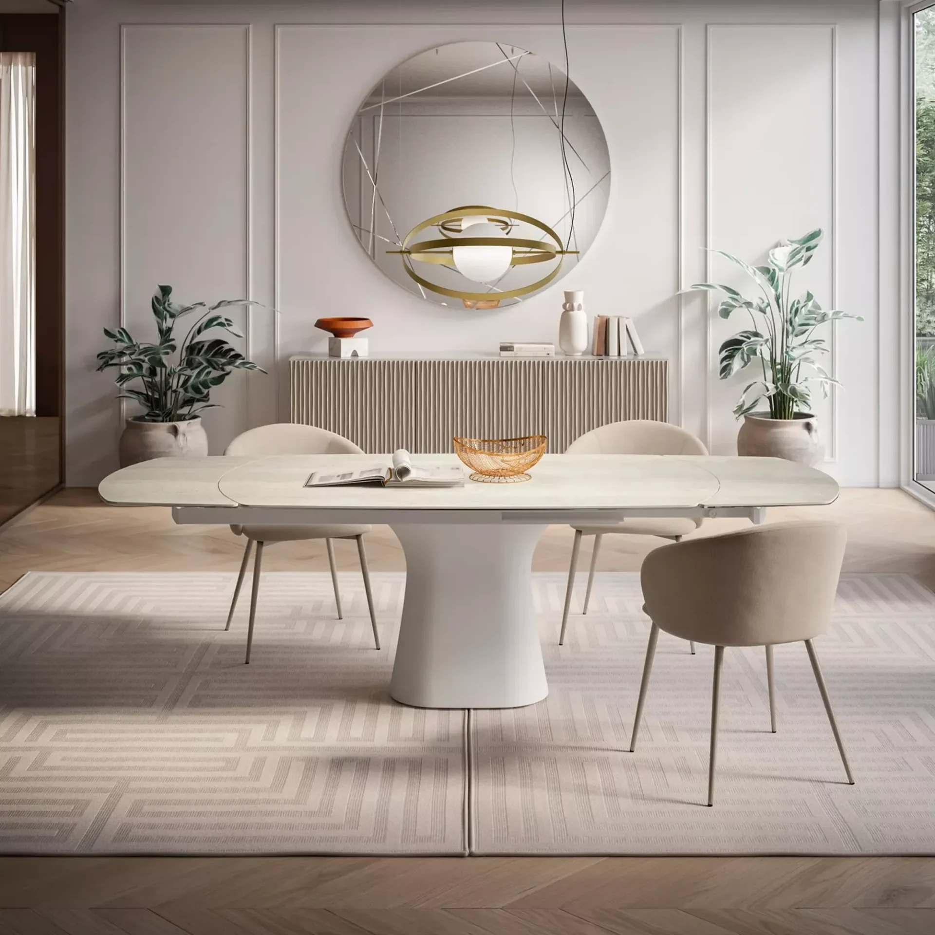 A modern dining room with a white oval table and light beige mesh chairs on a herringbone wood floor. A black marble fireplace is adorned with books and sculptures, with framed art above.