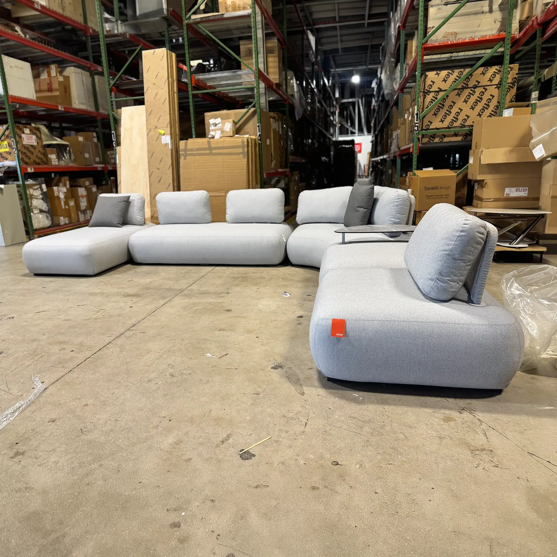 Modern outdoor sectional sofa with light gray cushions in warehouse setting.