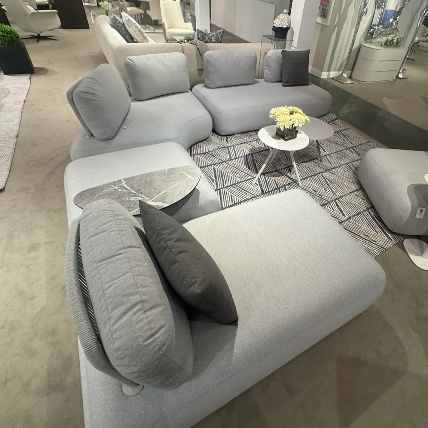 A light gray modular sofa with rounded edges, arranged on a geometric rug in a modern showroom setting.