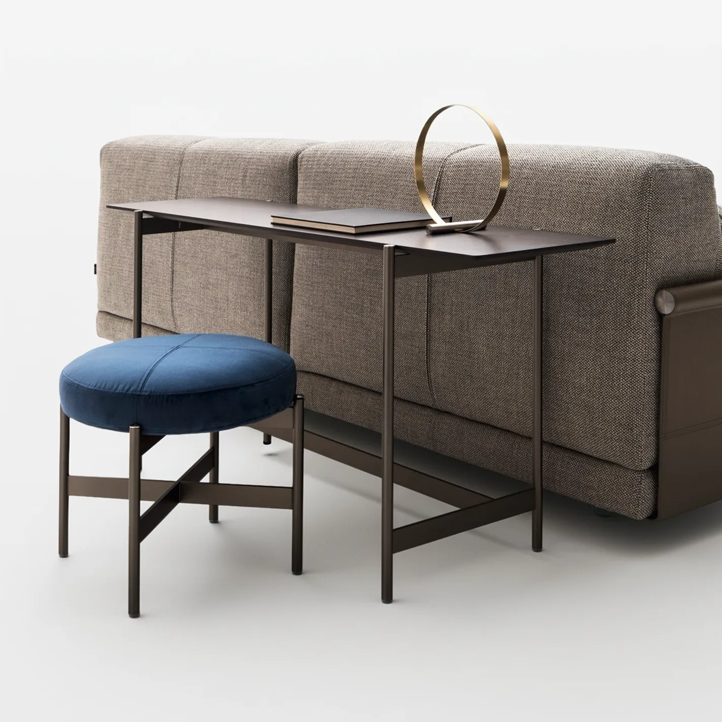 A modern living room setup with a brown sofa, a dark console table with a gold sculpture, and a blue velvet stool.