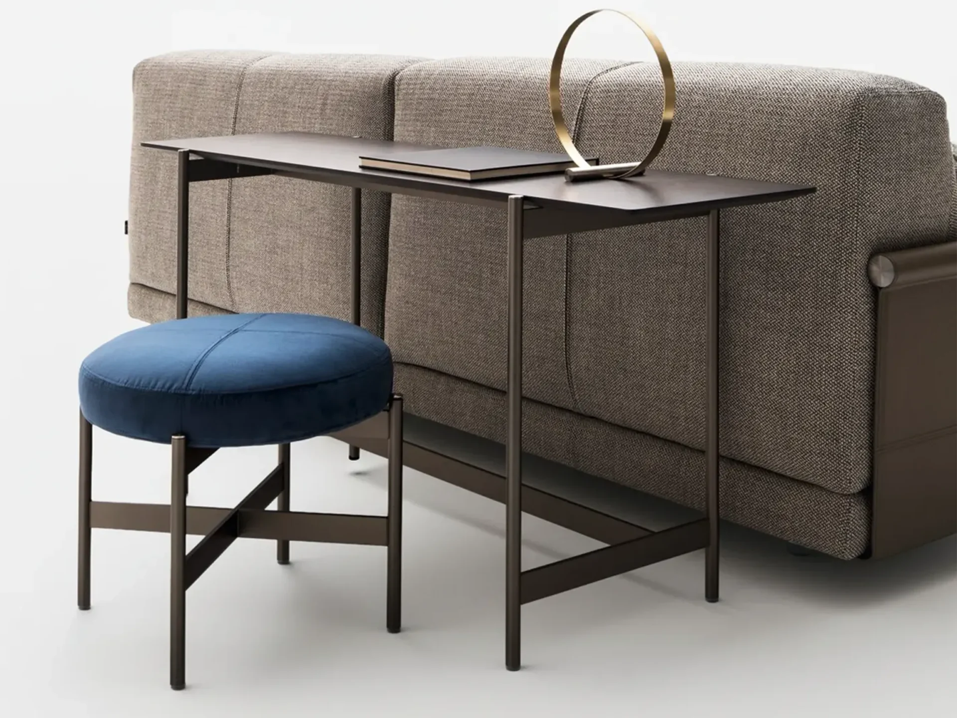 A modern console table with a book and gold decor, a blue velvet stool, and a textured beige sofa against a white background.