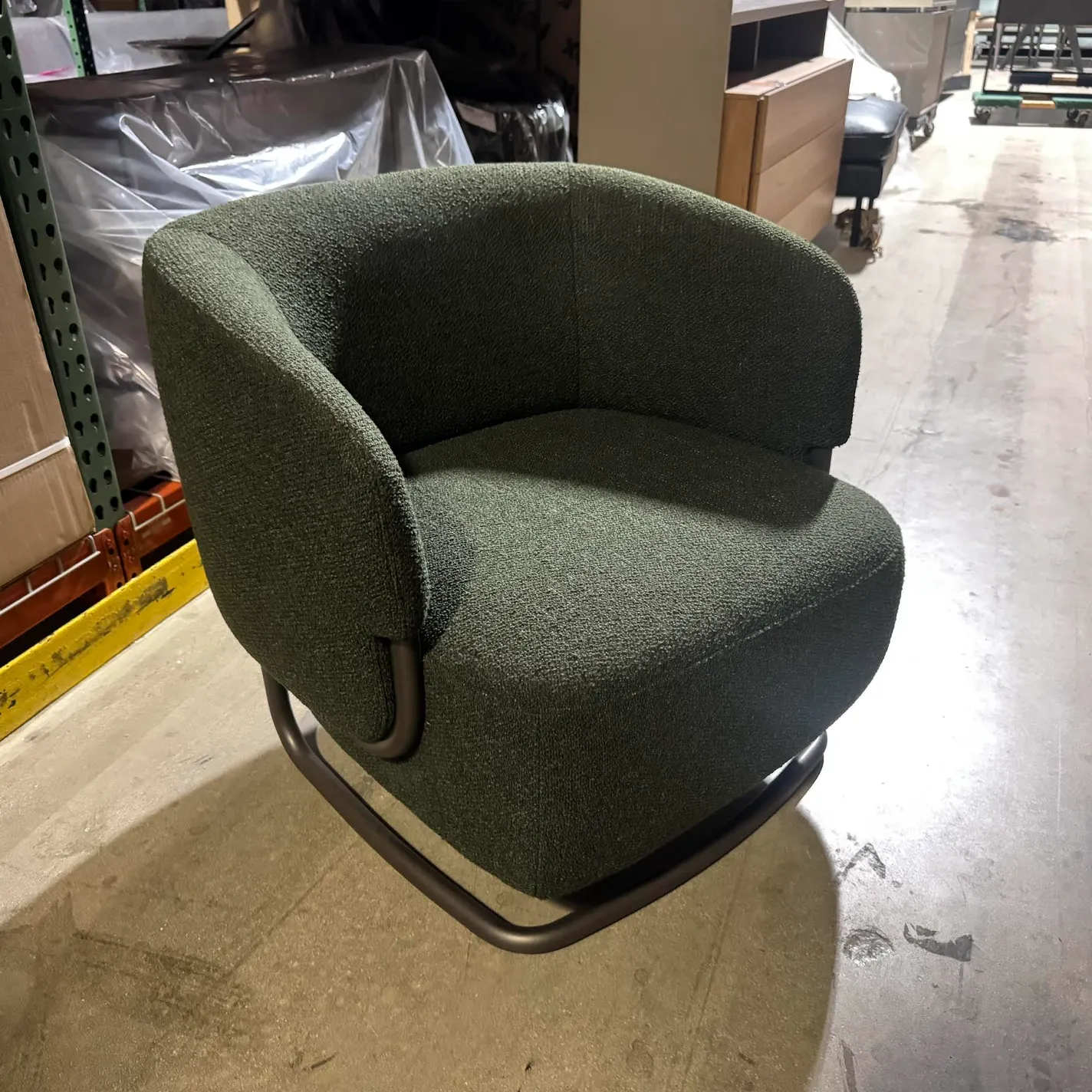 A dark green upholstered armchair with a rounded back and arms, sitting on a dark metal sled base on a concrete floor.