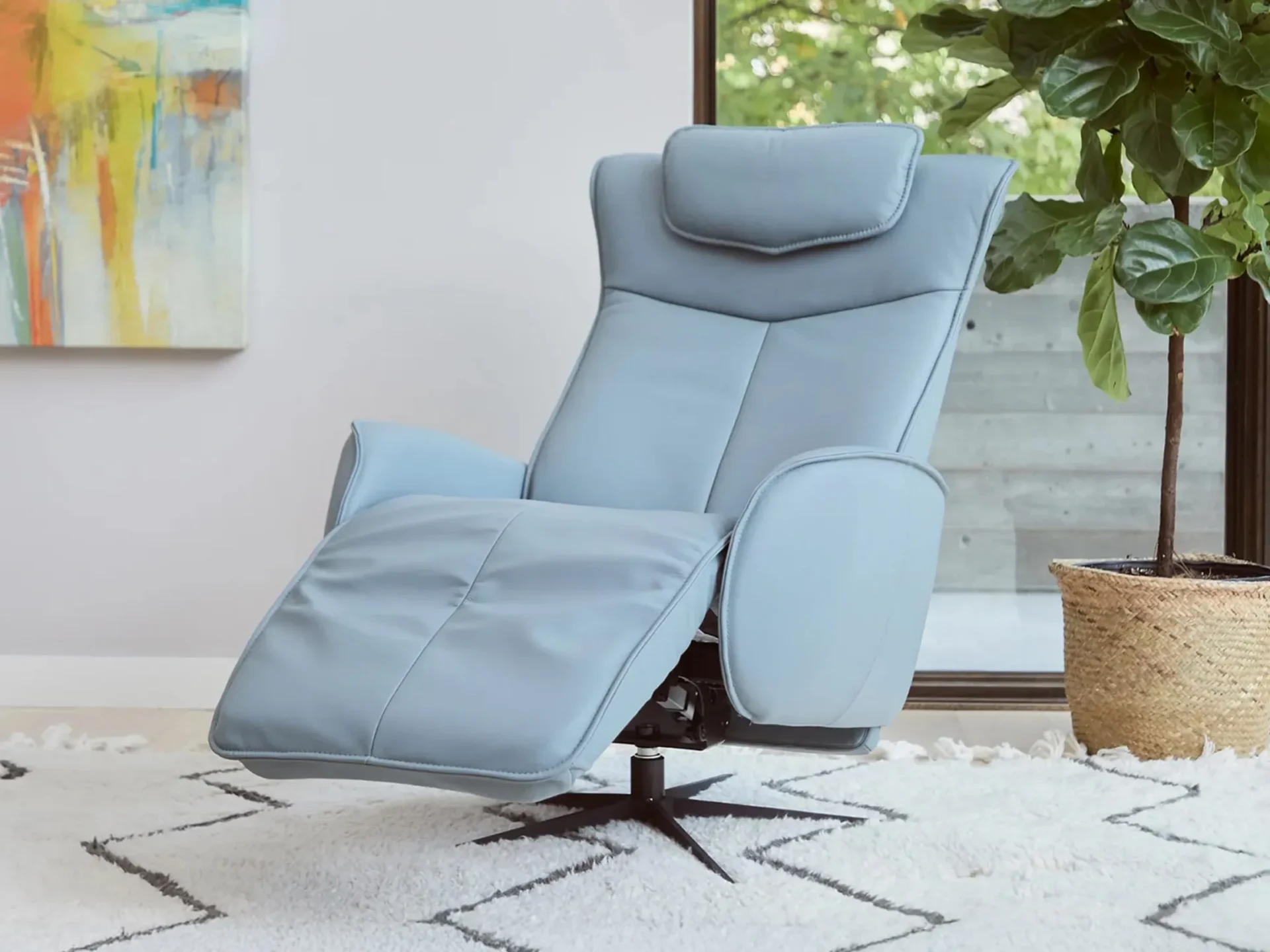 A light blue recliner chair in a reclined position on a white shag rug with a gray pattern. An abstract painting and a potted plant are in the background.