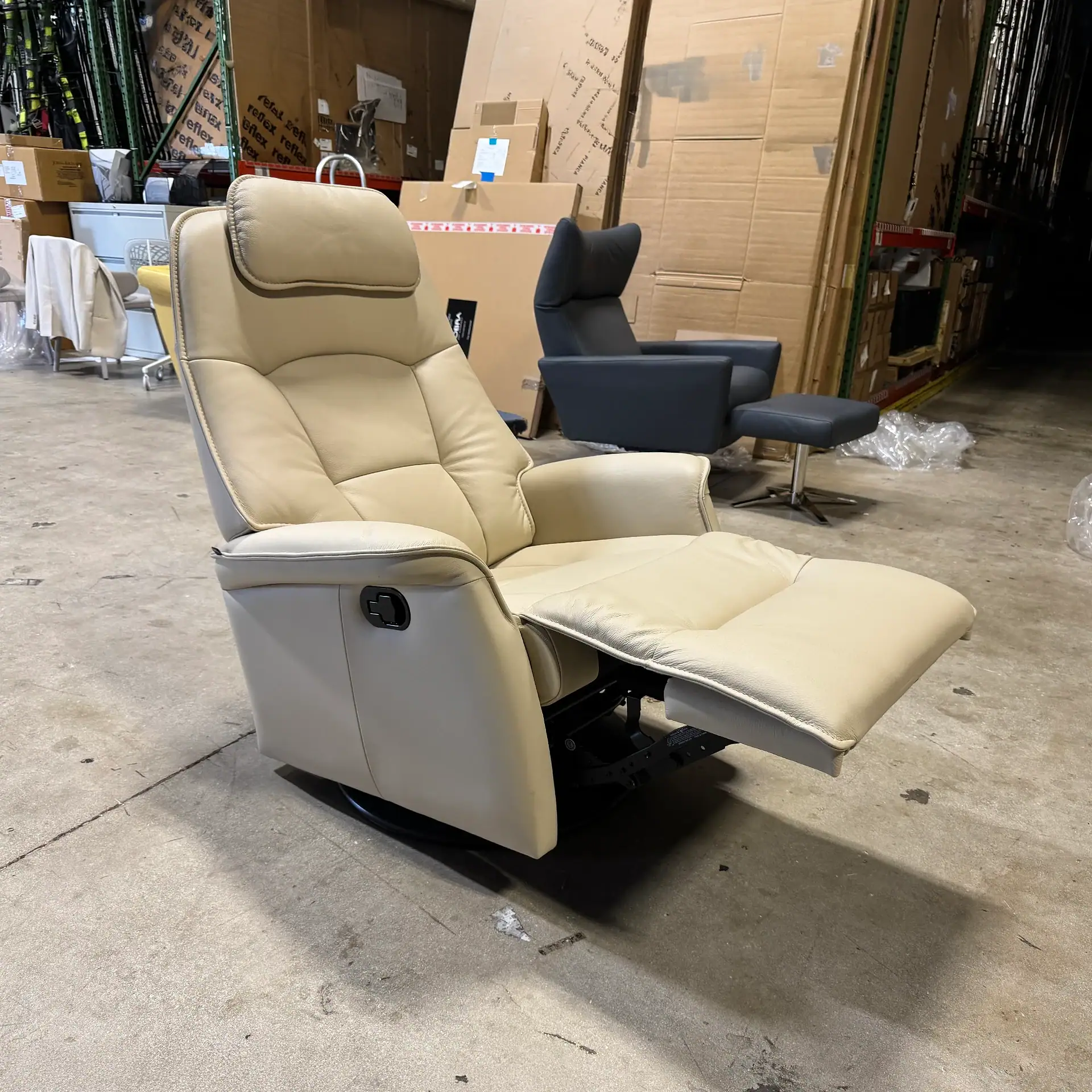 Cream-colored power recliner chair with adjustable headrest and footrest in warehouse setting.