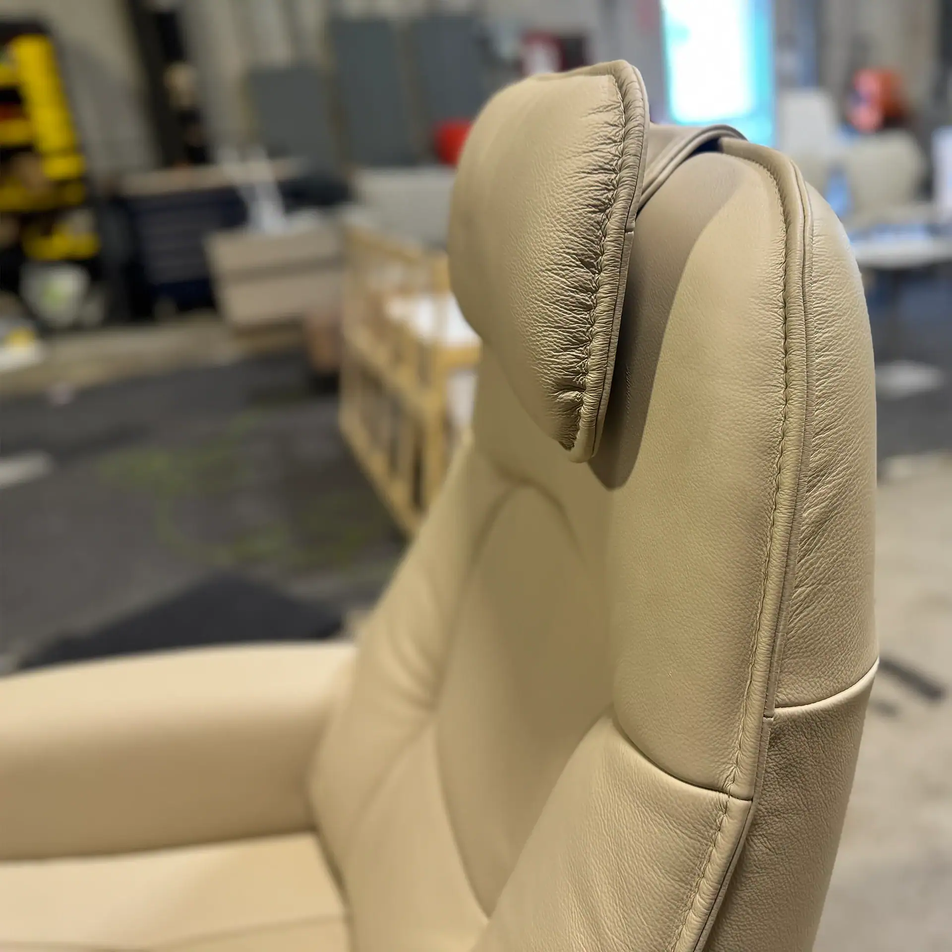 Cream-colored recliner chair with adjustable headrest in a showroom setting.