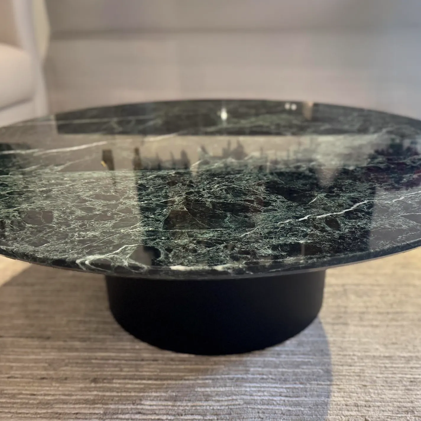 A round dark green marble coffee table with a black base, sitting on a light-colored textured rug.