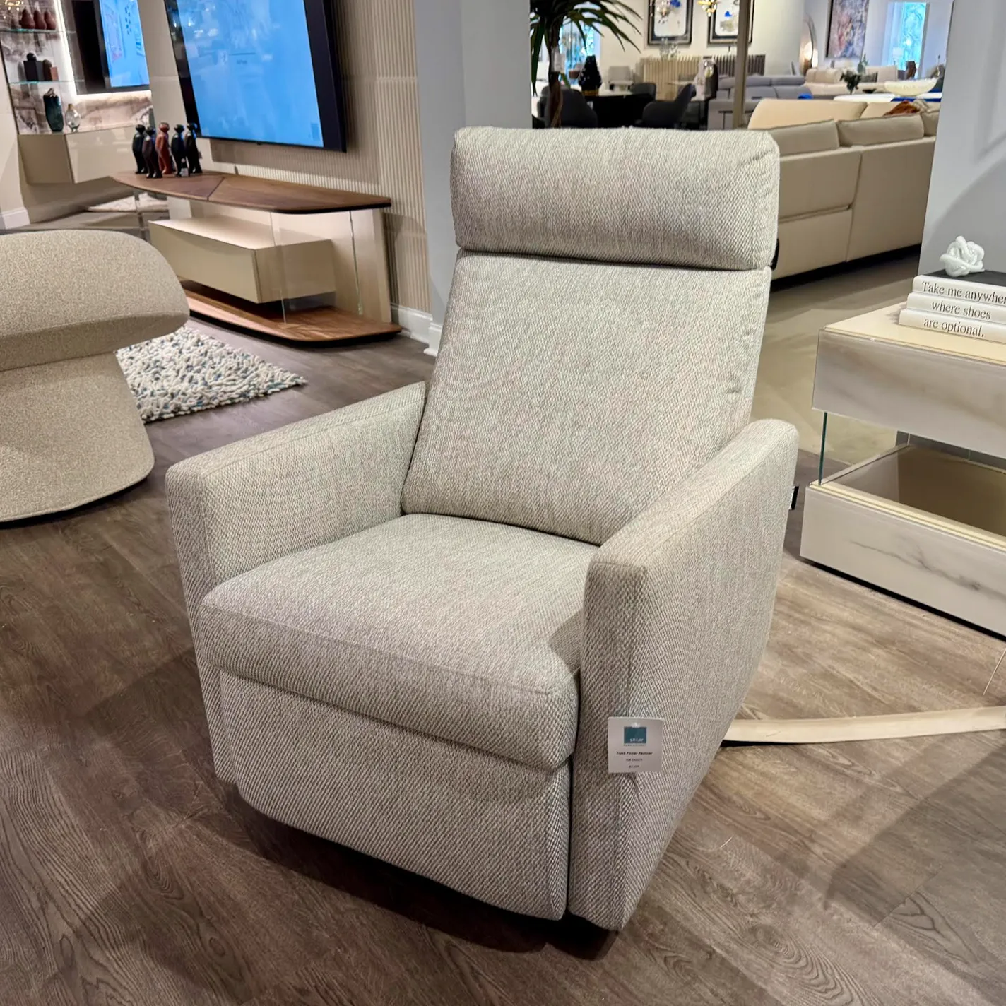 A light grey, modern fabric recliner chair in a furniture showroom.