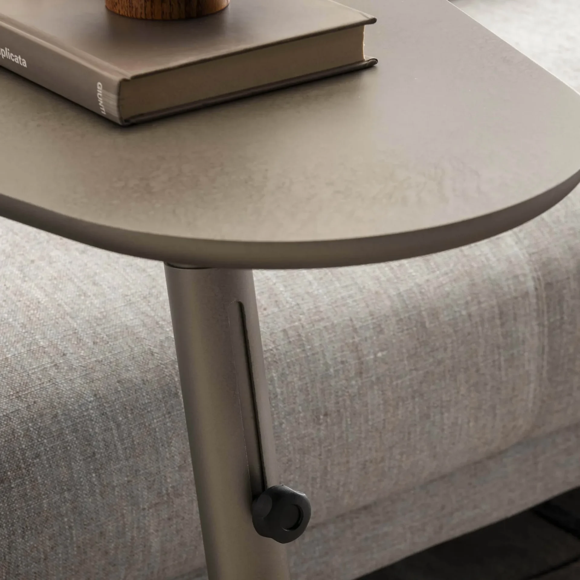 A taupe, height-adjustable side table with a book on top, next to a light gray upholstered sofa.