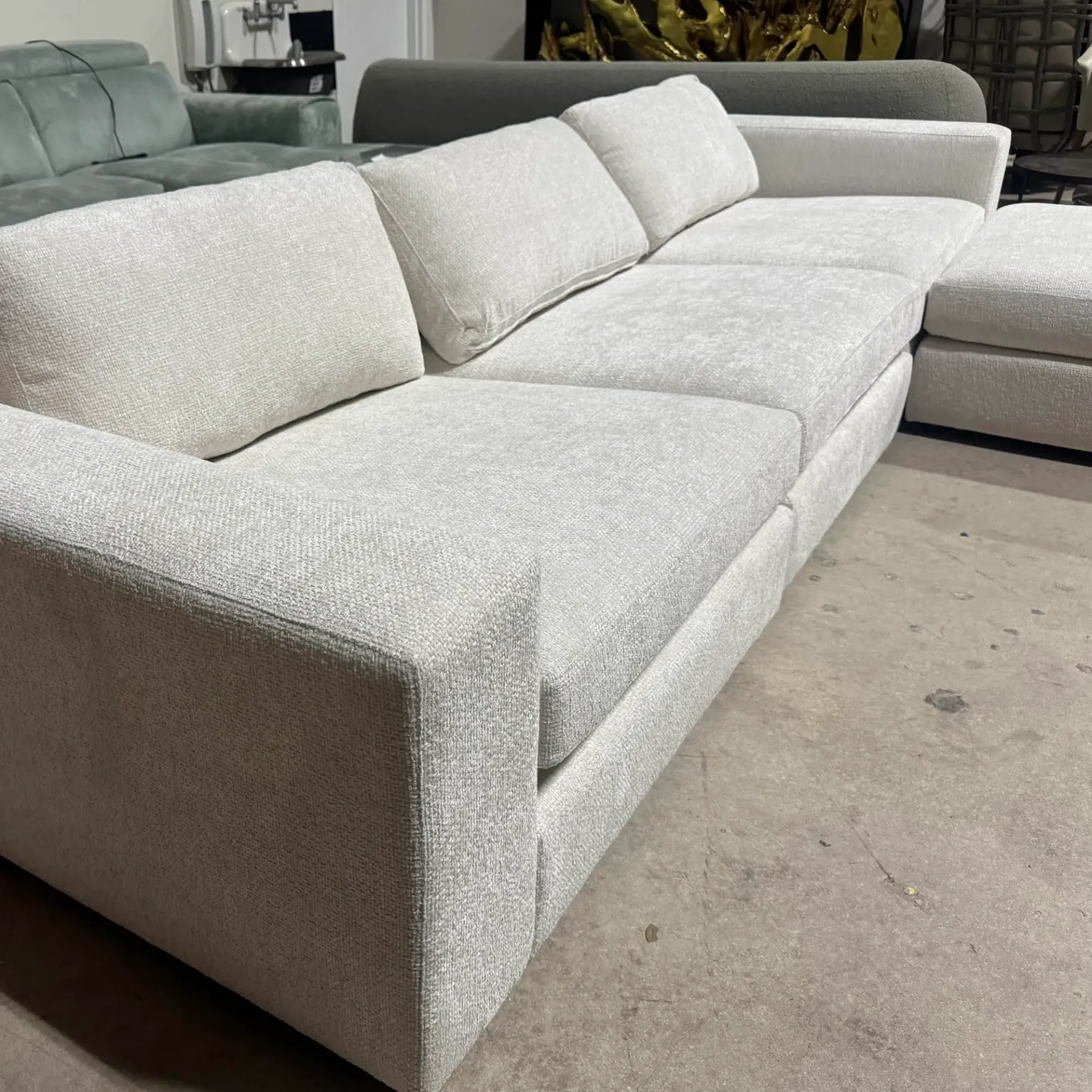 A large, light grey L-shaped sectional sofa on a concrete floor, with other furniture visible in the background.