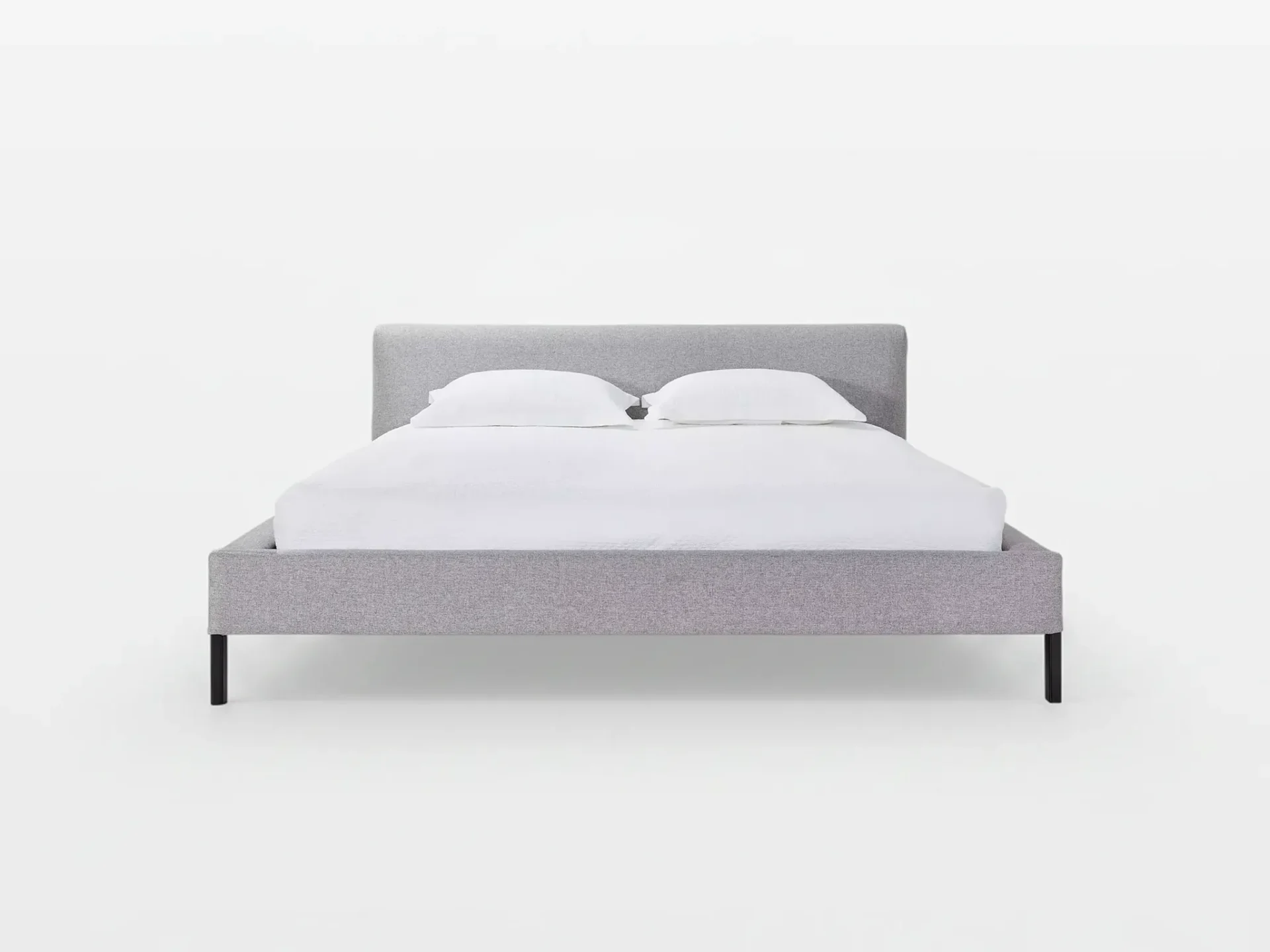A light gray upholstered platform bed with a headboard, white sheets, and two white pillows on a white background.