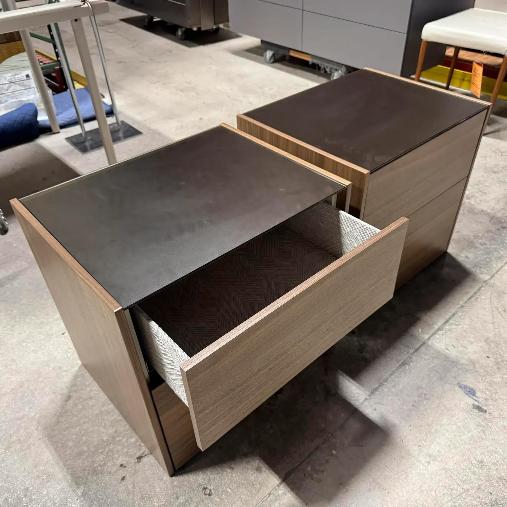 Two modern wooden nightstands with dark tops on a concrete floor. One drawer is open, showing a patterned interior.
