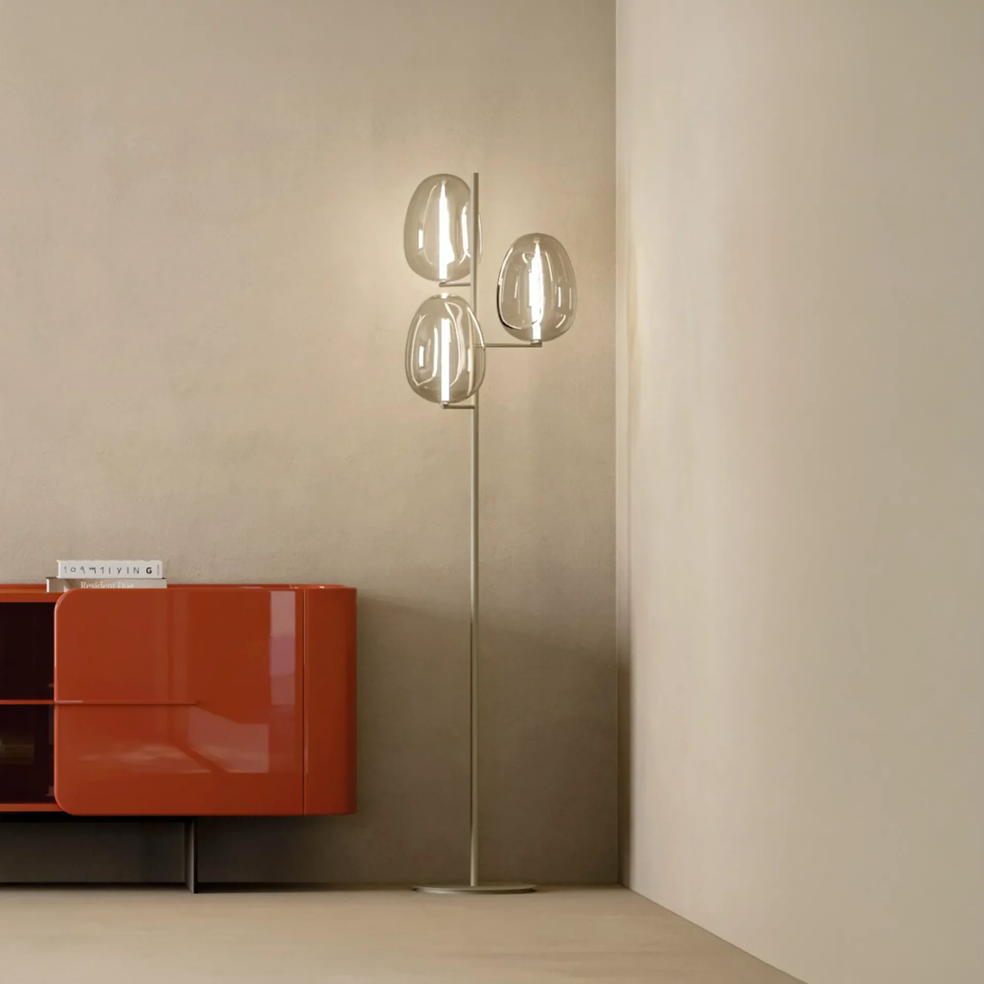 A modern floor lamp with three oval glass shades stands next to a glossy orange cabinet in a minimalist room.