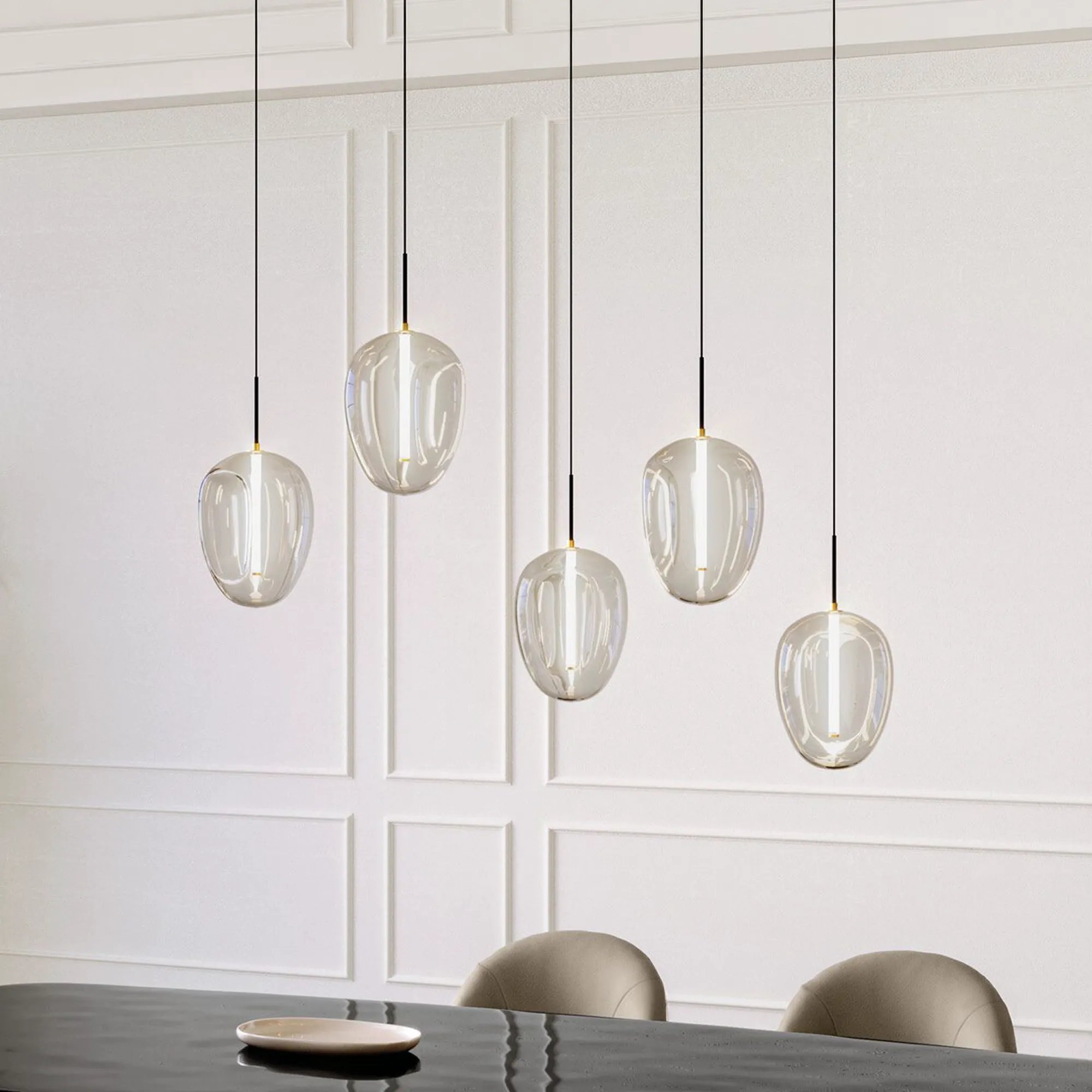Five modern, clear glass pendant lights with internal vertical illumination hang over a dark, reflective dining table. The white paneled wall and upholstered chairs are visible in the background.