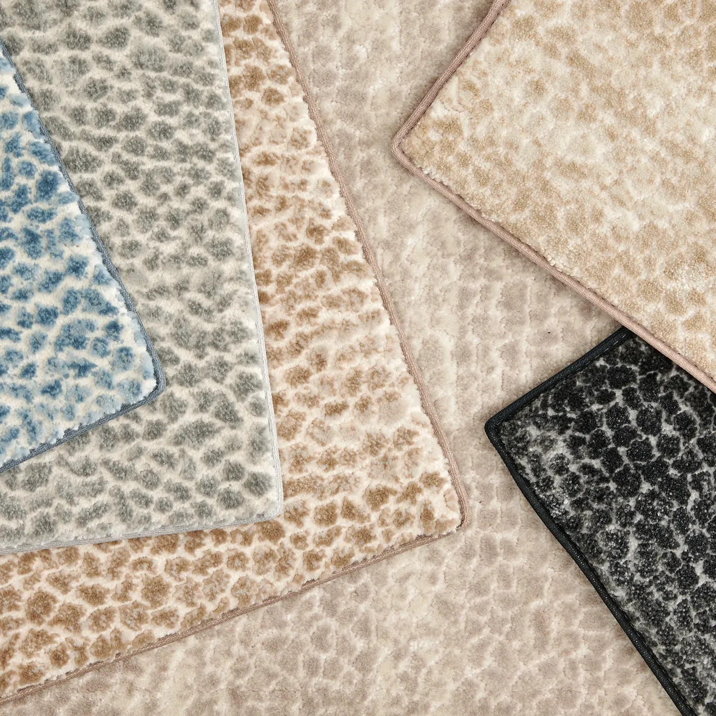 Five overlapping carpet samples in blue, gray, light brown, beige, and black, all with a subtle, mottled pattern.