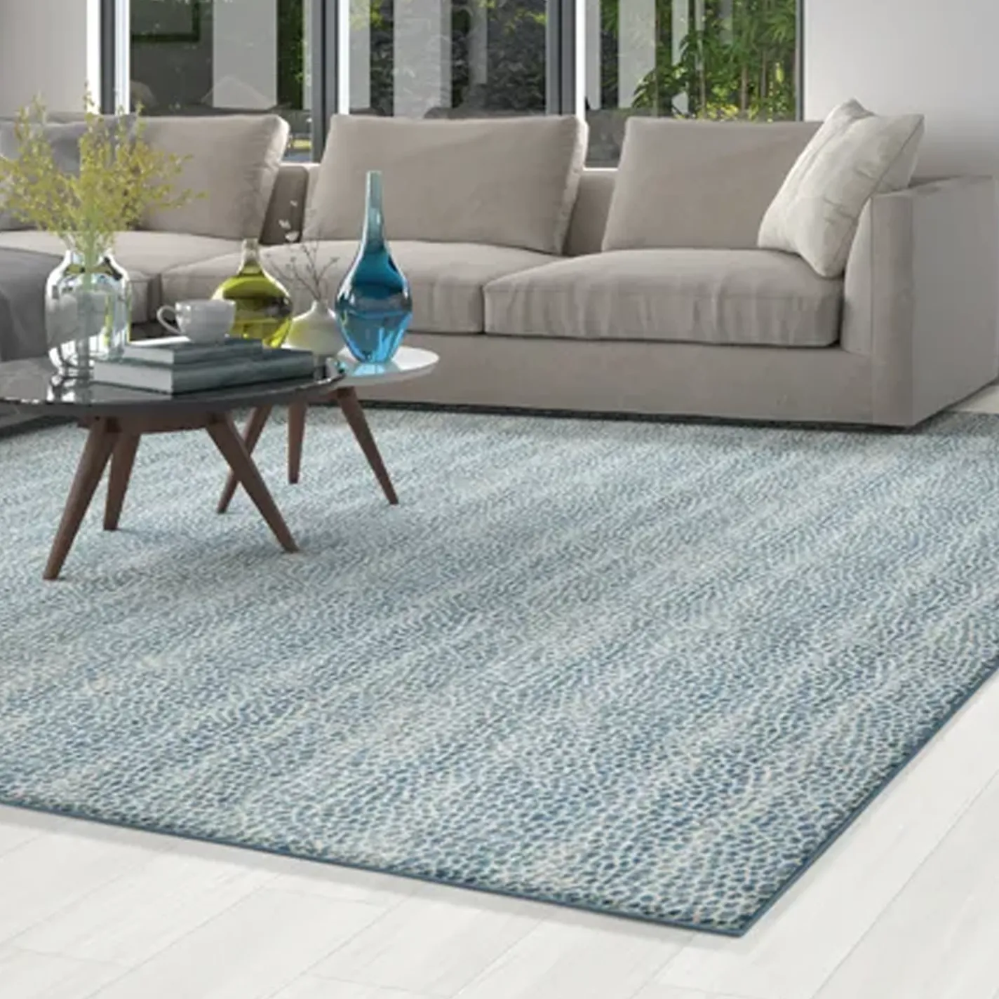 A modern living room with a light blue and white patterned area rug, a beige sectional sofa, and a coffee table adorned with colorful glass vases and books.
