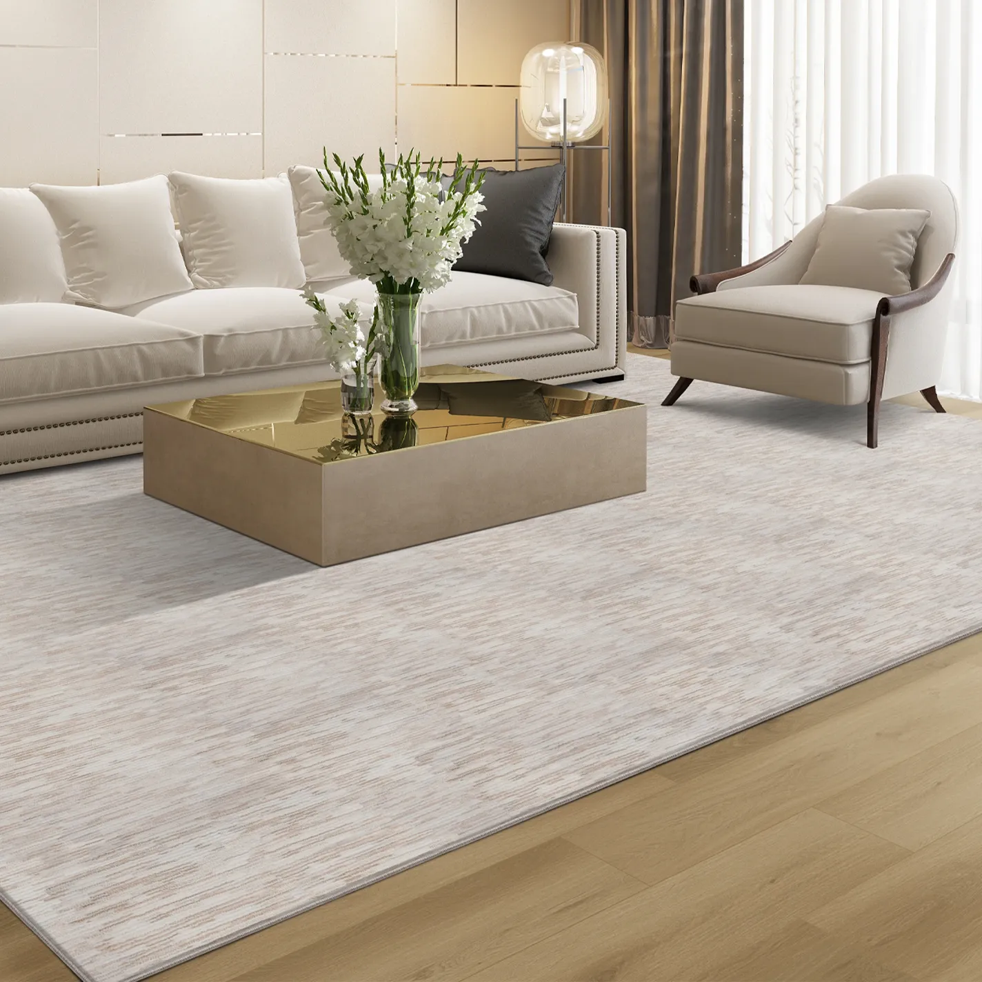 A modern, elegant living room with an off-white sofa, armchair, gold coffee table with white flowers, and a textured area rug on a hardwood floor.