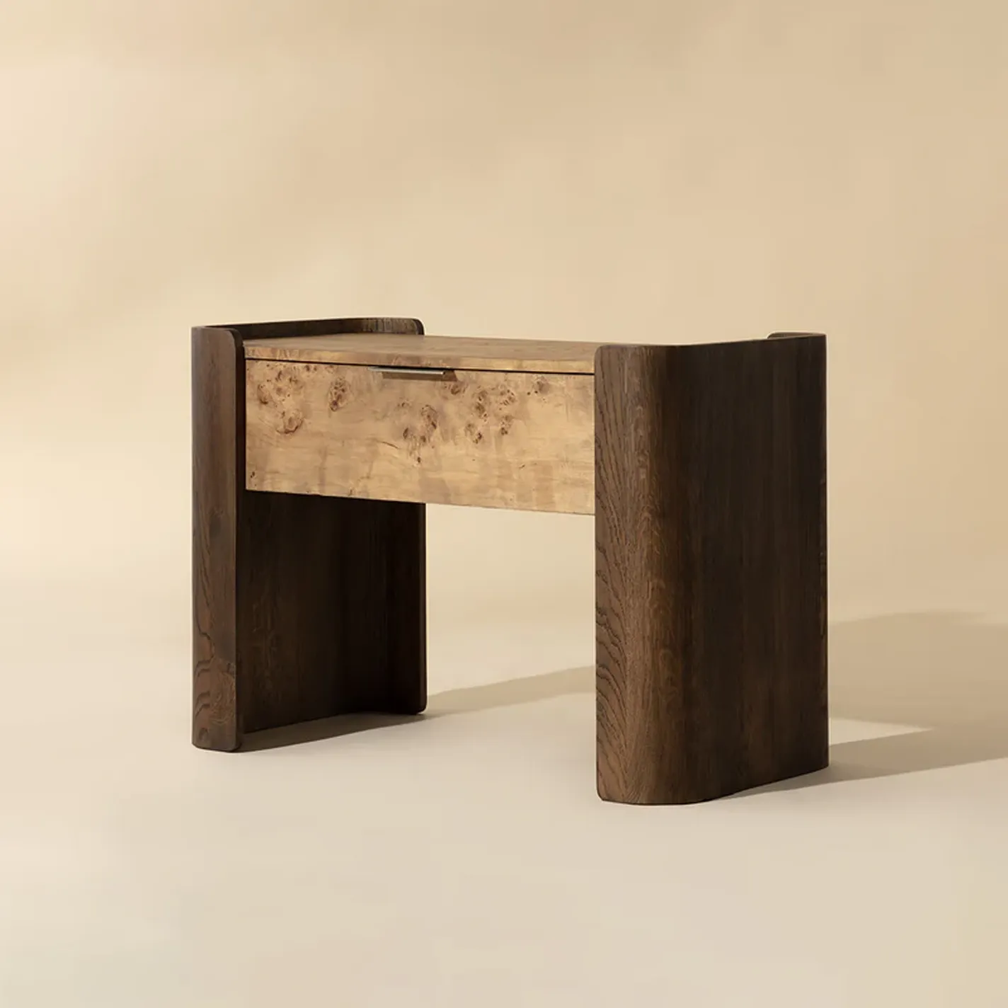 A modern console table with a dark U-shaped wood frame and a lighter burl wood drawer, set against a light beige background.