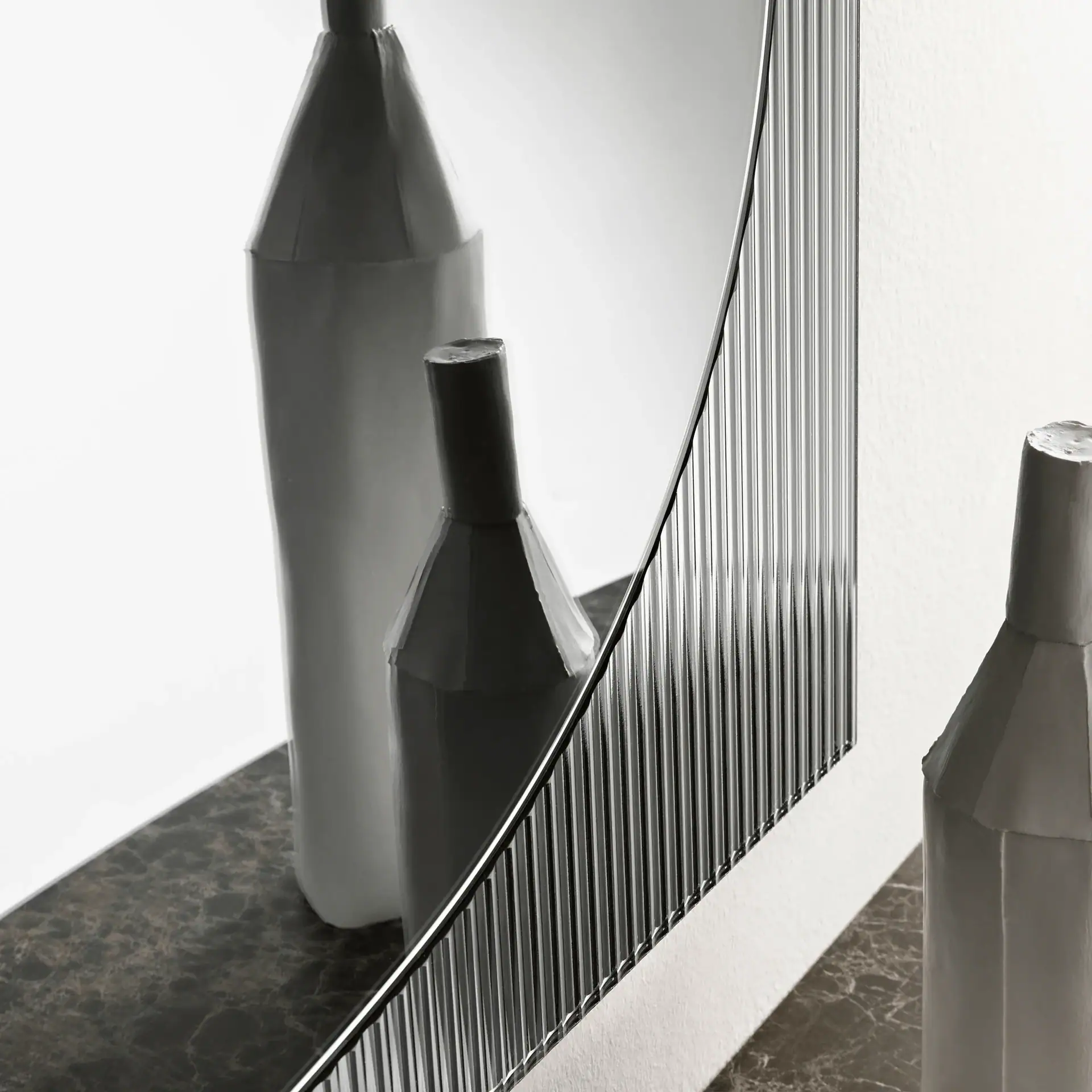 Elegant wall mirror with a curved design, paired with stylish vases for contemporary decor.